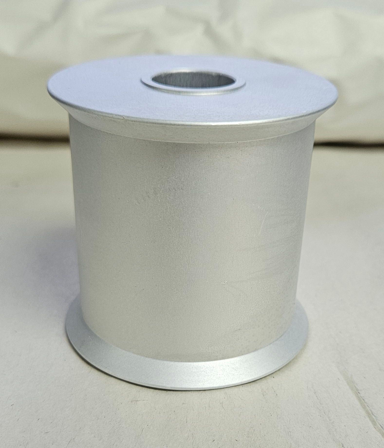 A light gray, cylindrical metal spool with a circular opening at the top, standing on a neutral surface.