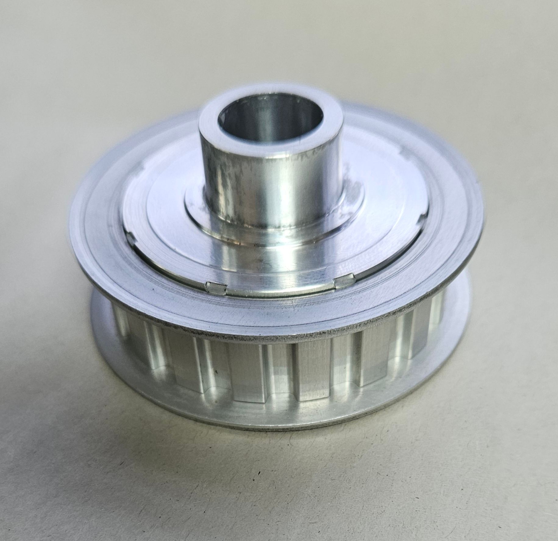 A silver metal timing belt pulley with a center bore and flange, set against a plain, neutral background.