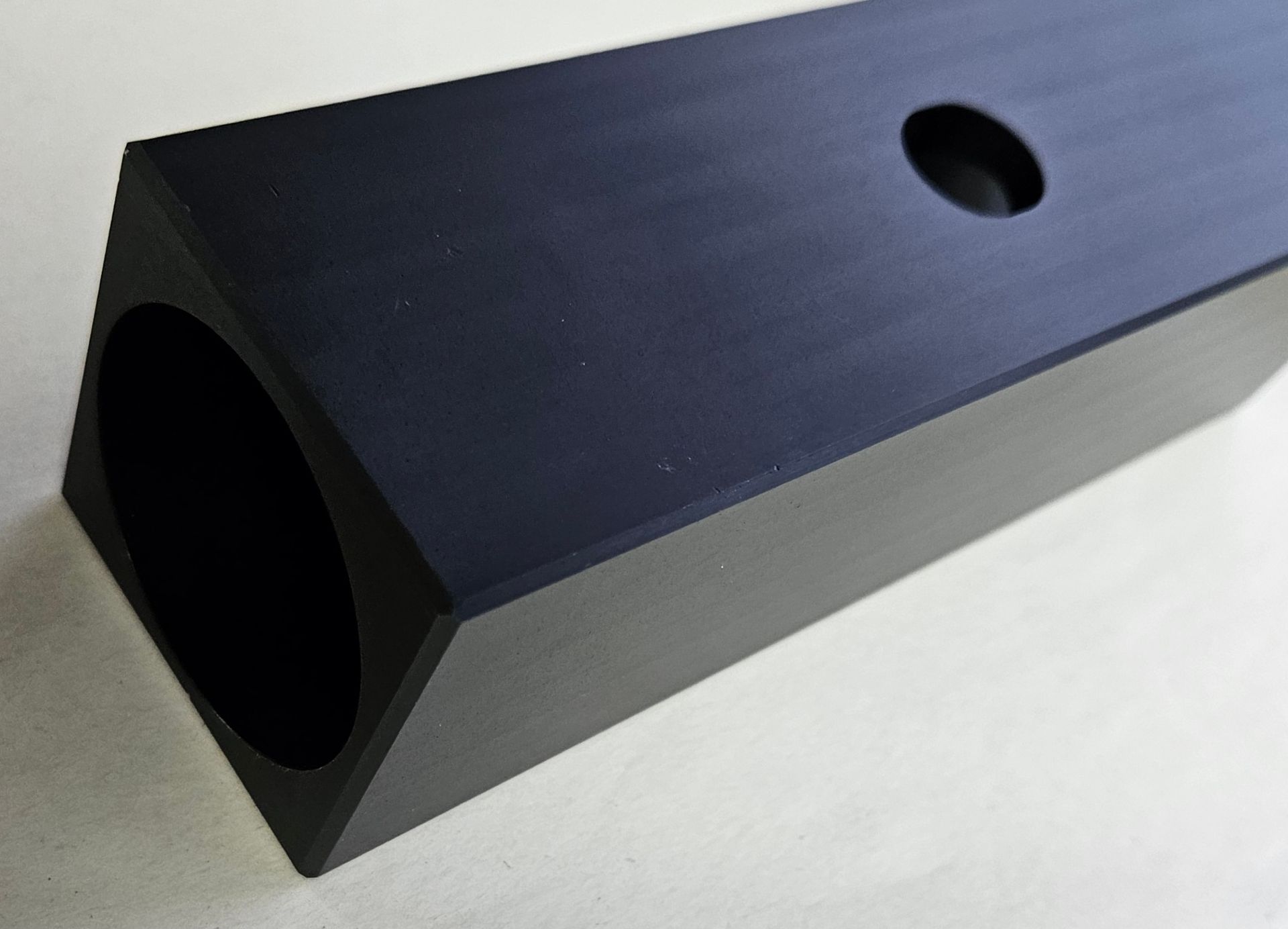 A matte black, triangular aluminum extrusion bar with a large circular bore and a smaller hole on the top flat surface.