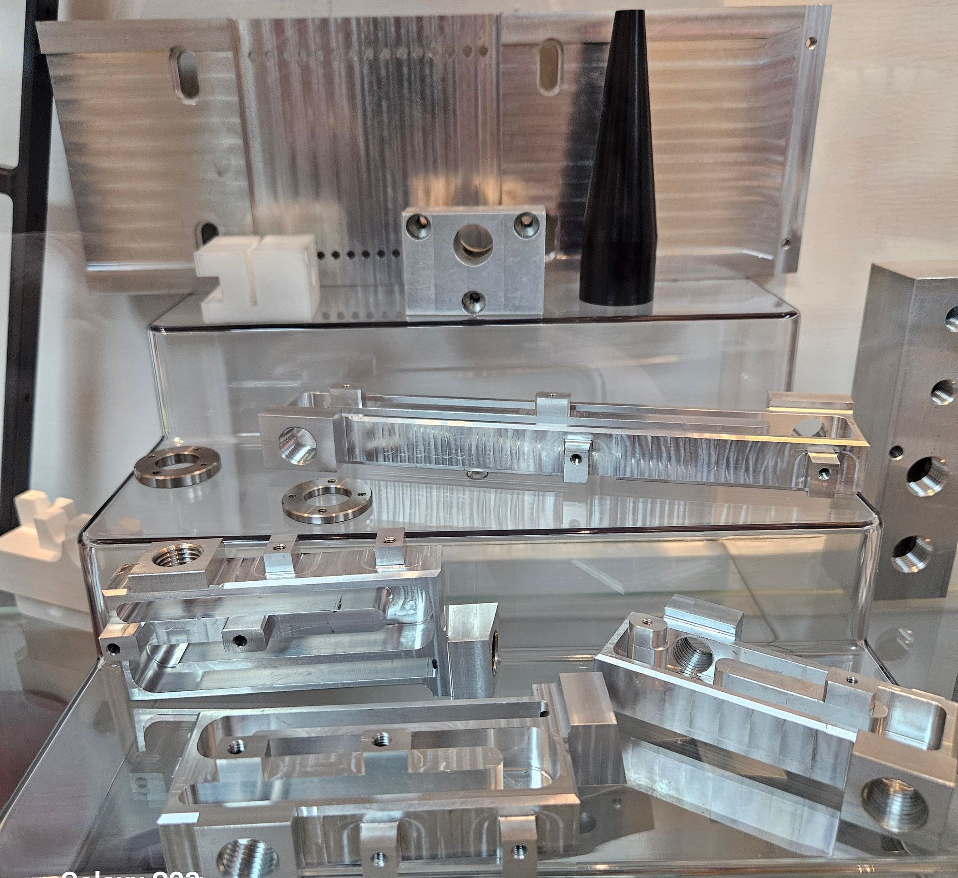 A display of various precision-machined metal and plastic industrial components arranged on glass shelves.