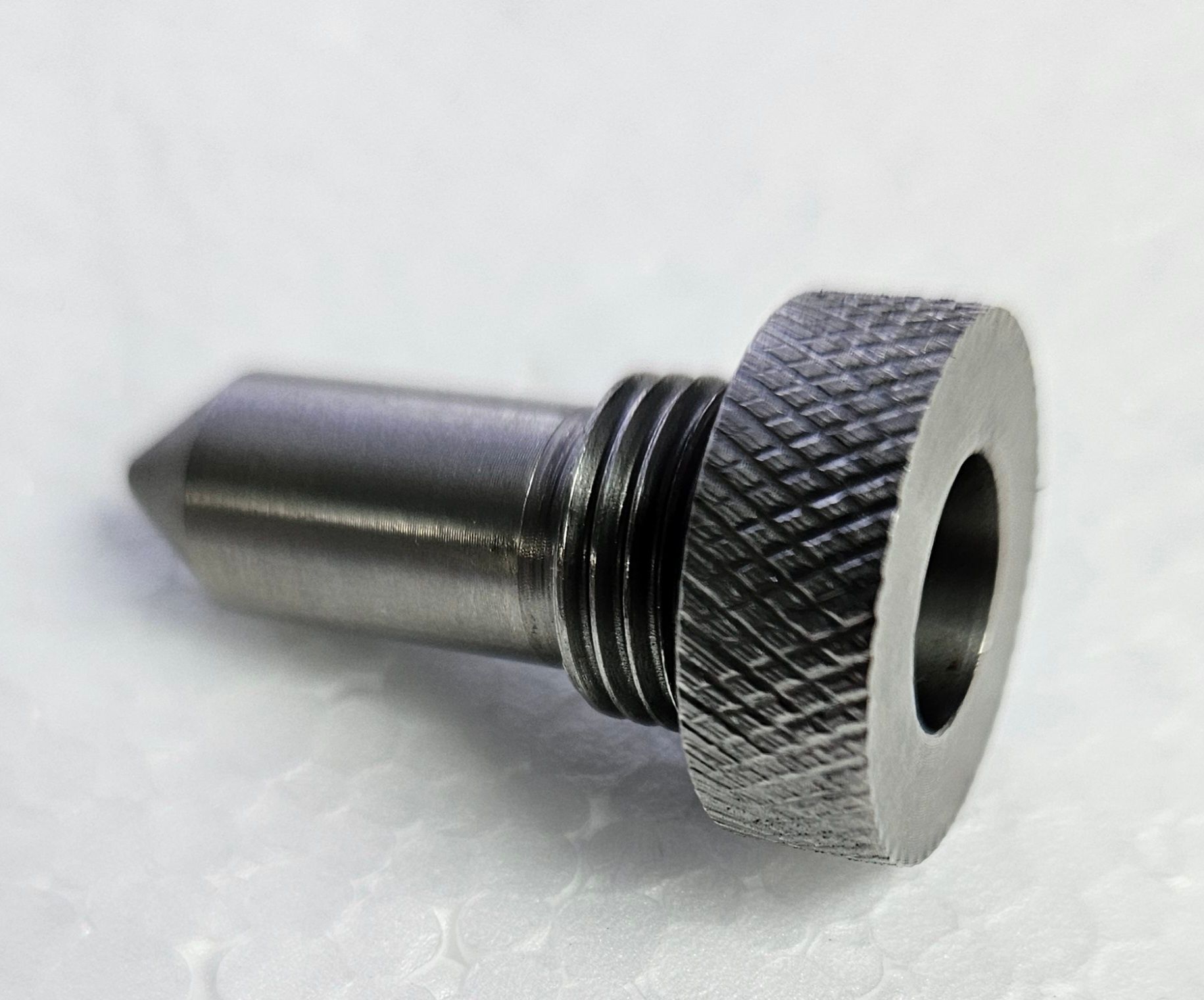 A close-up of a small, metallic, pointed indexing plunger with a knurled head and threaded shaft.