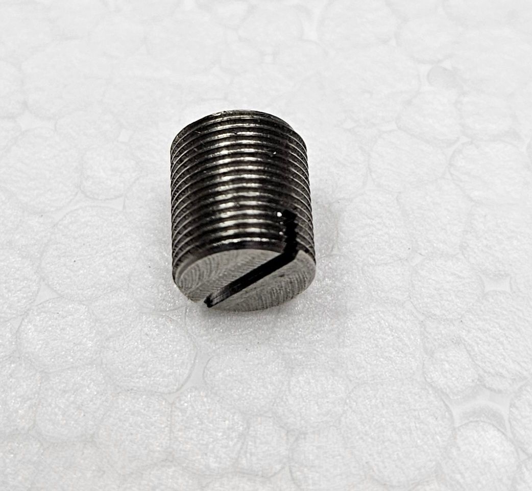 A metal set screw with a slotted head for a flat-head screwdriver, sitting on a white, textured surface.