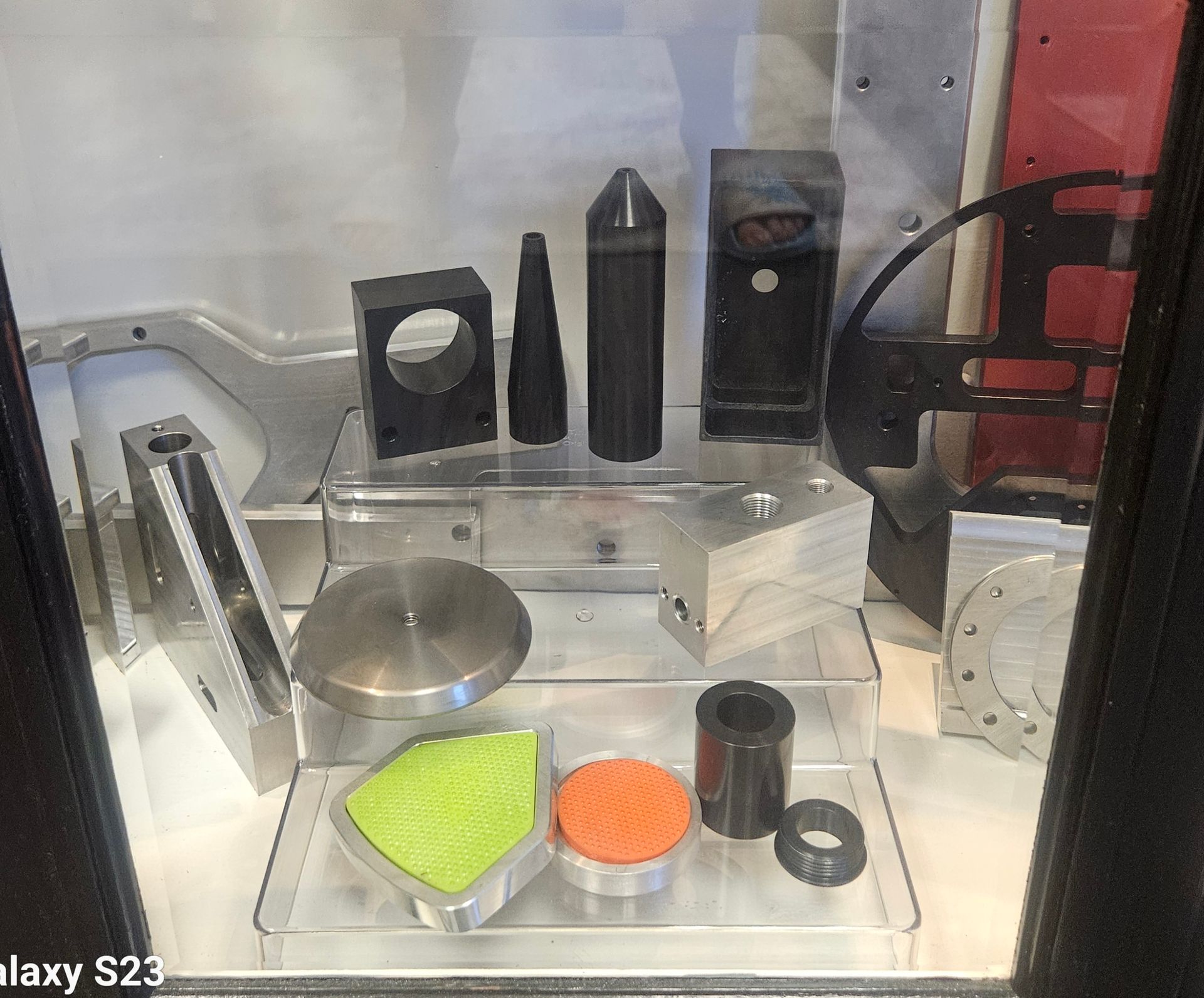 A display case showcasing an assortment of industrial-style 3D printed components and metal machined parts.