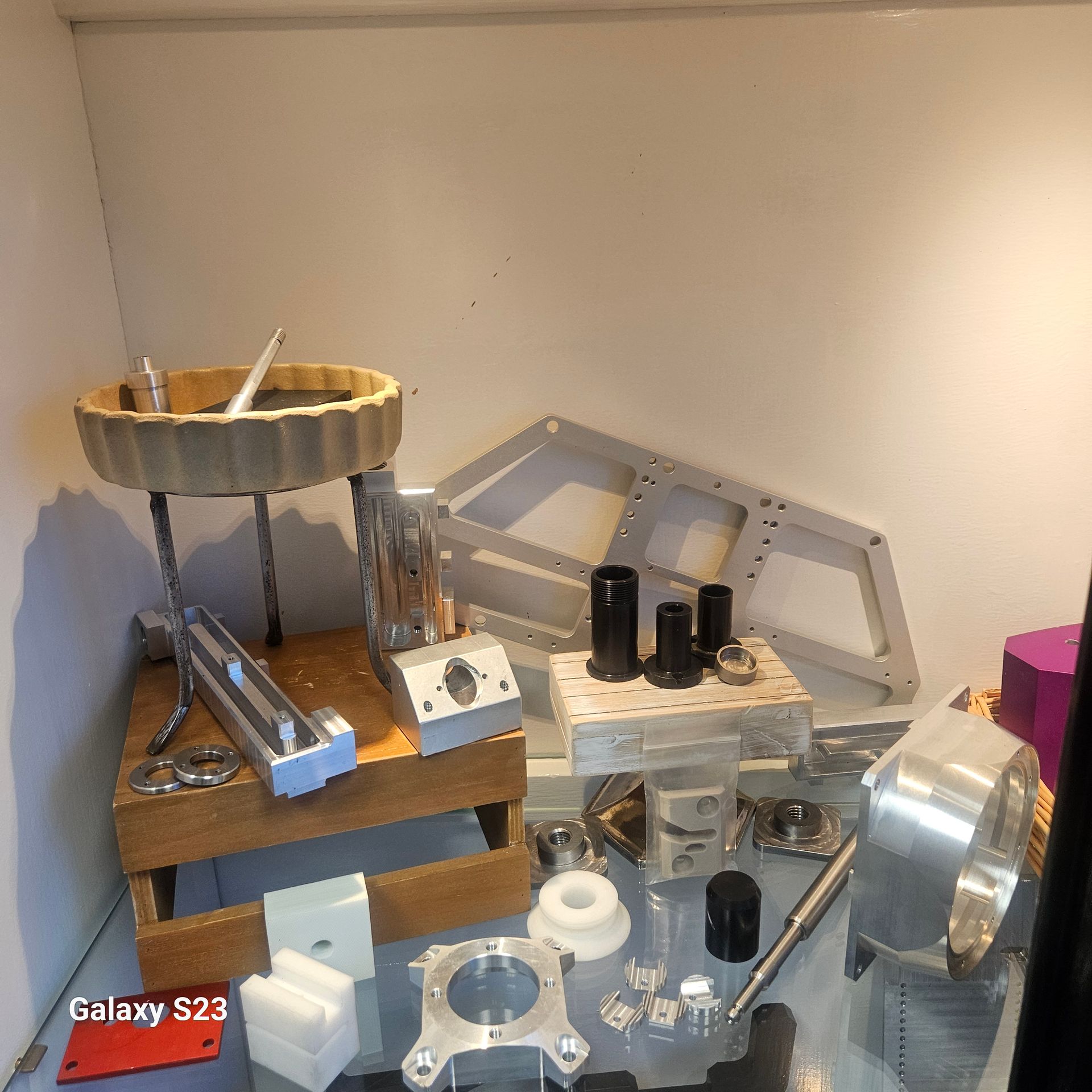 A collection of various metal and plastic manufactured machine parts displayed on a wooden stand and a shelf.