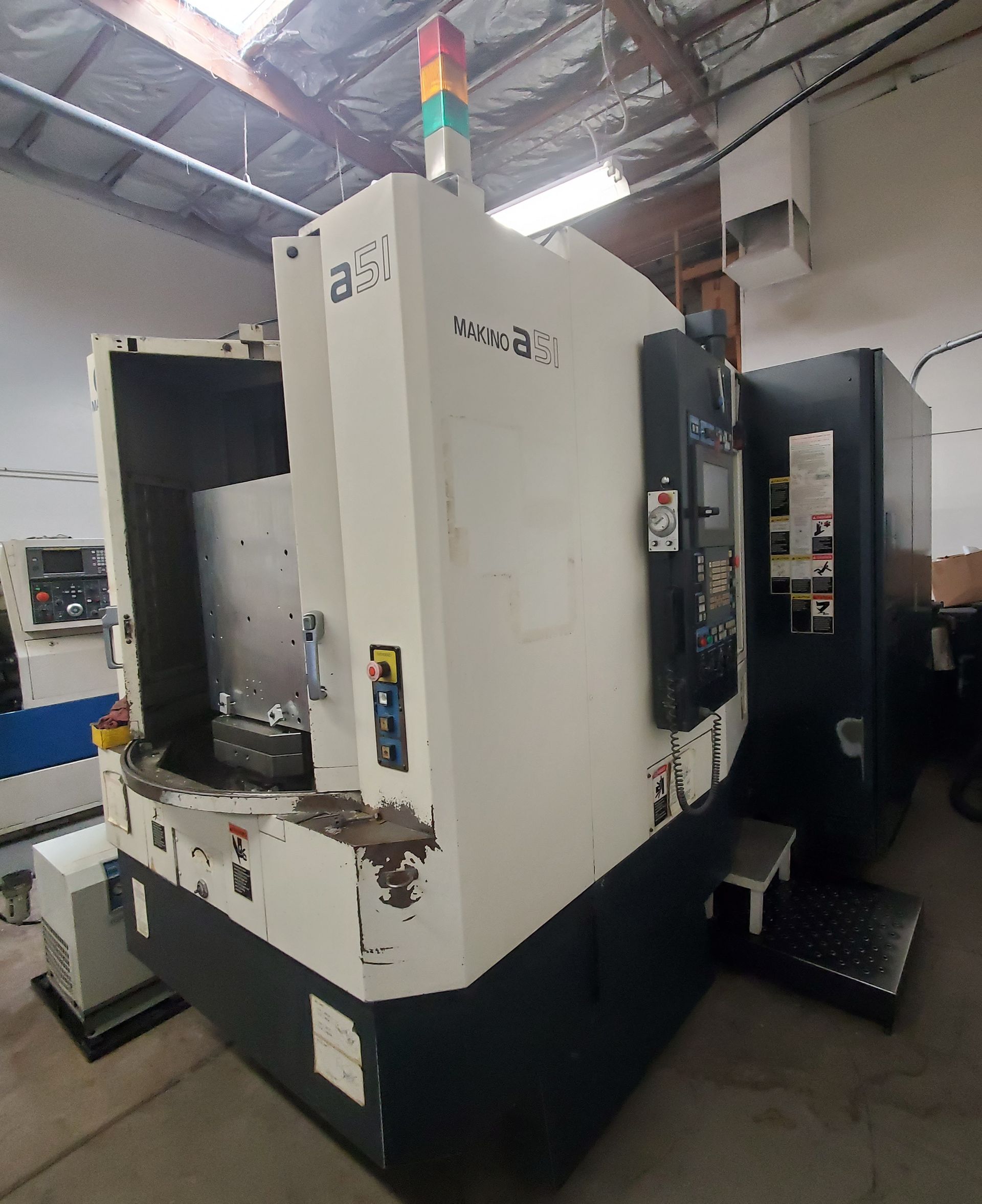 A white and dark gray CNC milling machine stands in a workshop with a warning signal light on top.