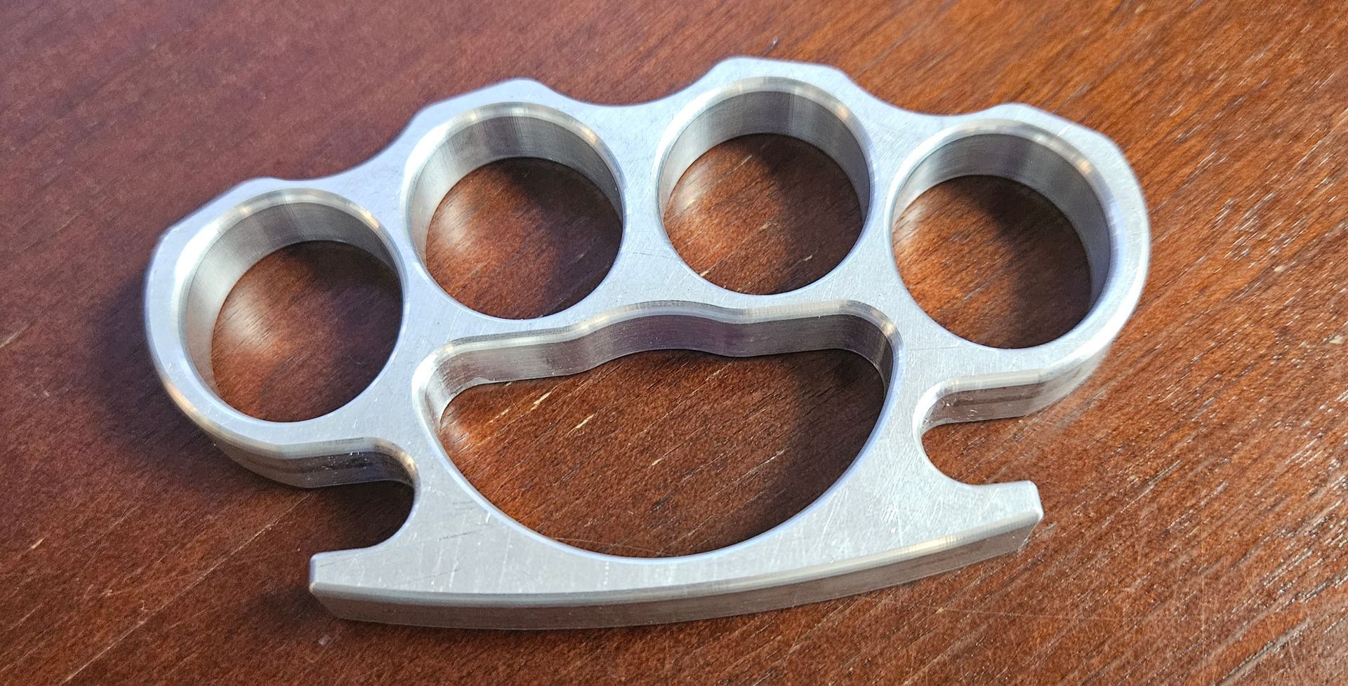 A silver-colored metal knuckle duster lying on a polished wooden surface.