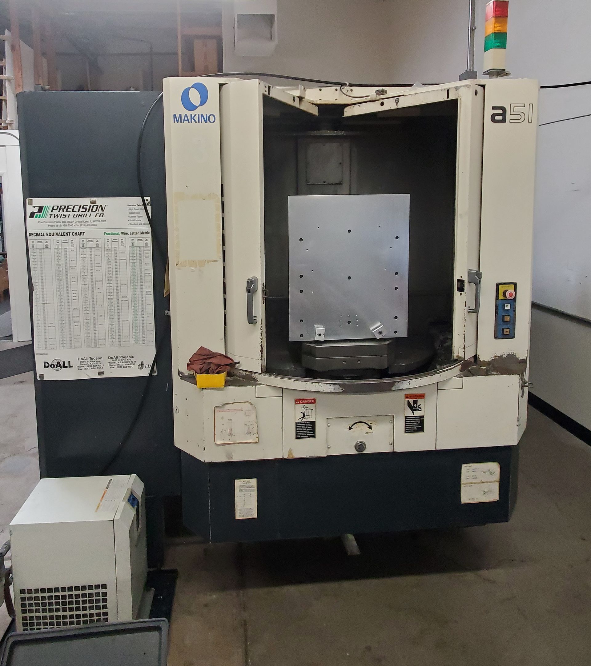 A cream and dark gray industrial CNC milling machine sits in a workshop with a metal plate mounted inside its open doors.