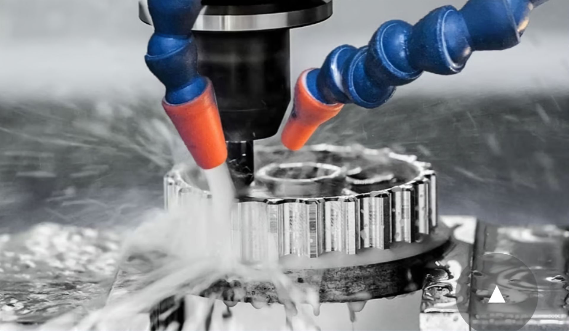 A CNC machine cutting a metal gear while blue and orange nozzles spray cooling fluid onto the workpiece.