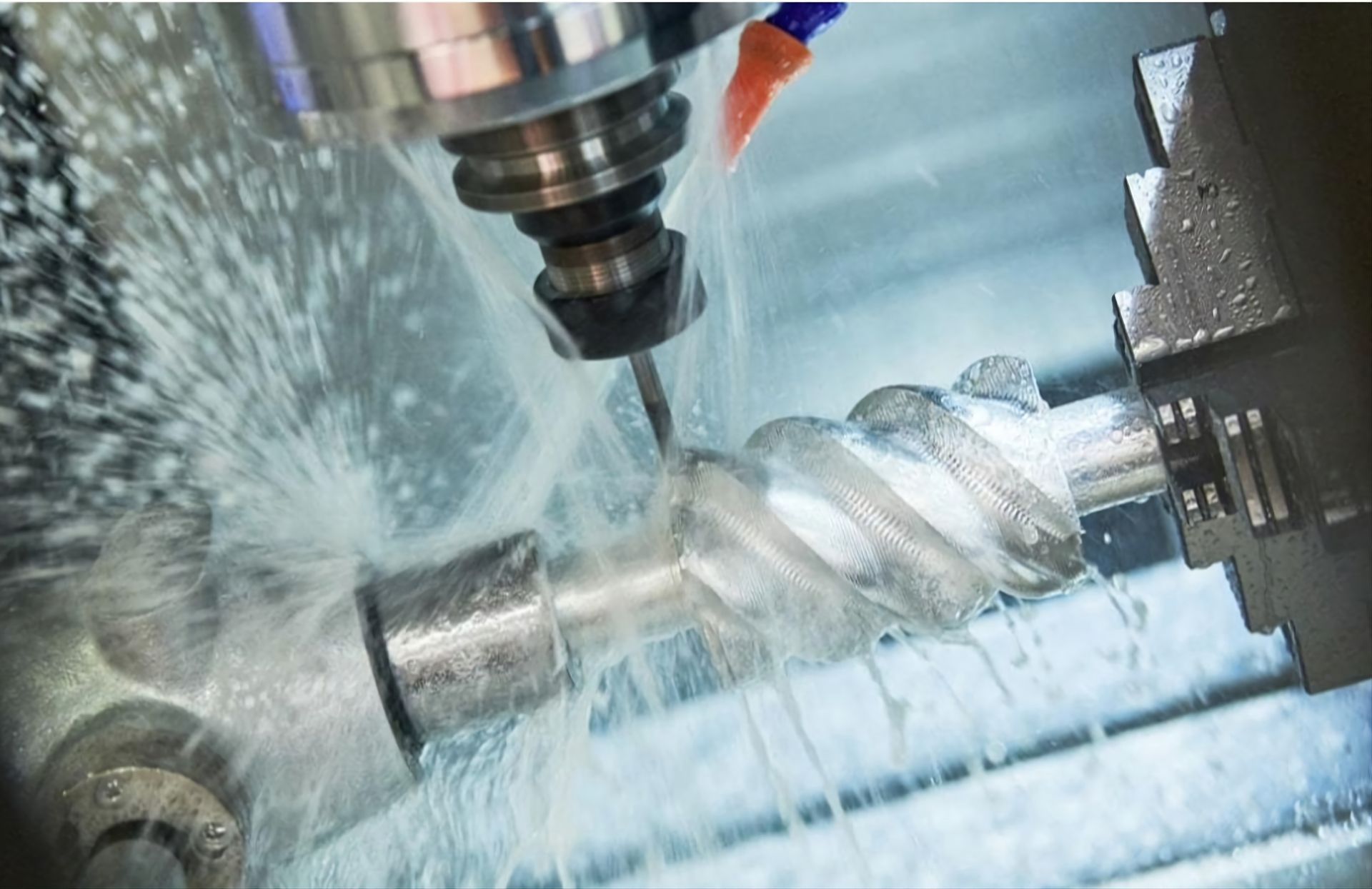 A CNC milling machine cuts a metal screw while liquid coolant sprays over the part during the manufacturing process.
