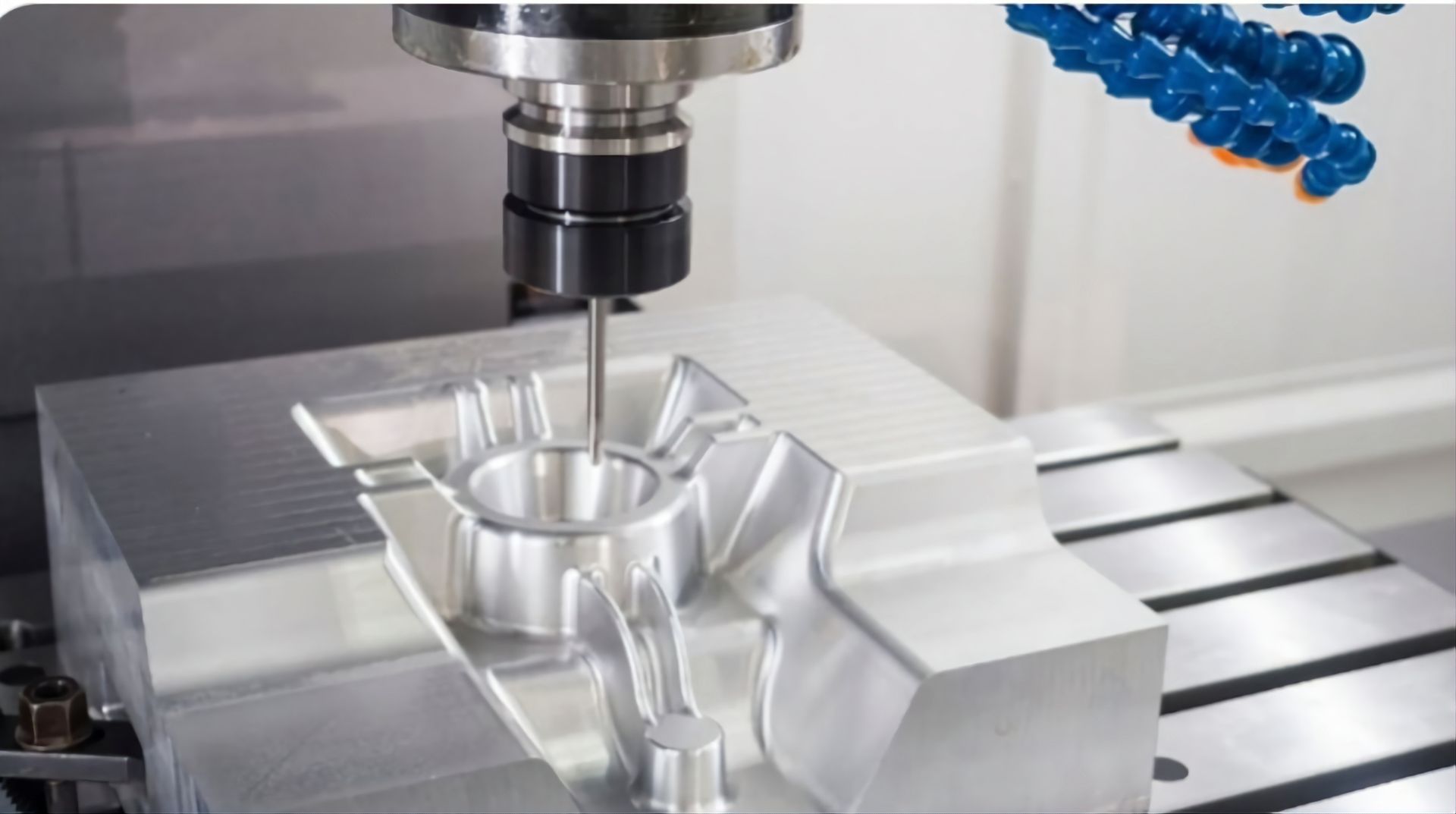 A CNC milling machine cuts a complex shape into a silver metal block on a work table.