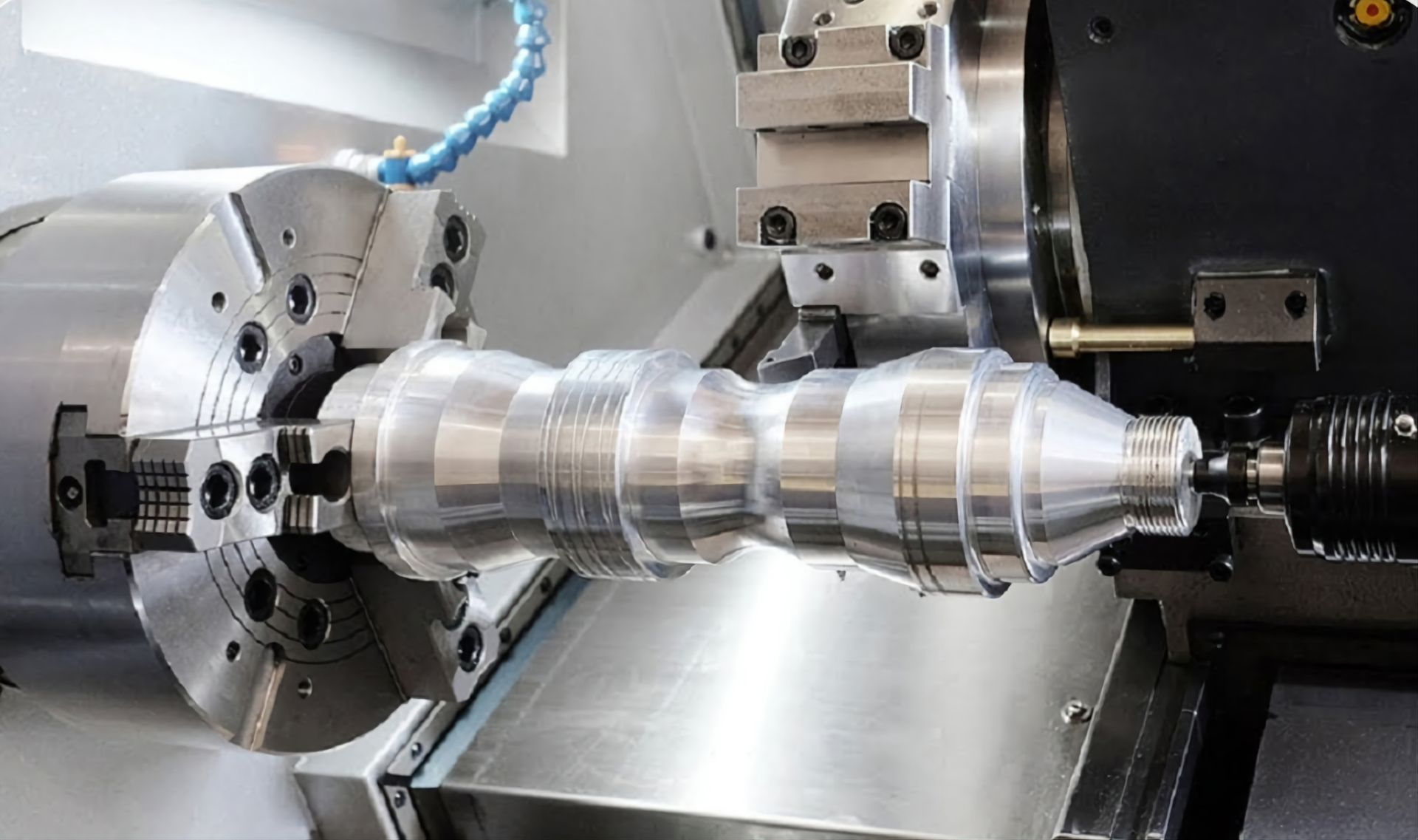 A CNC lathe machine cutting a shaped metal workpiece held between a chuck and a tailstock center.