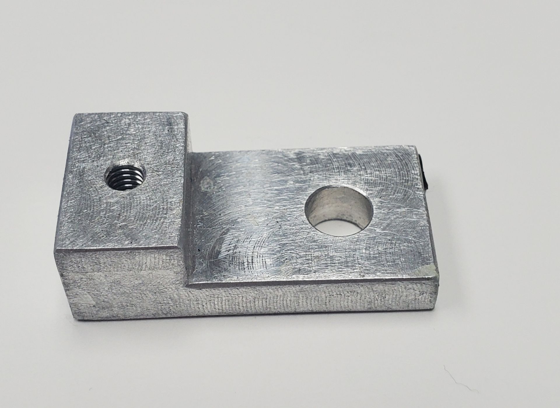 A metallic, L-shaped mounting bracket with a threaded hole on one side and a larger circular hole on the flat section.