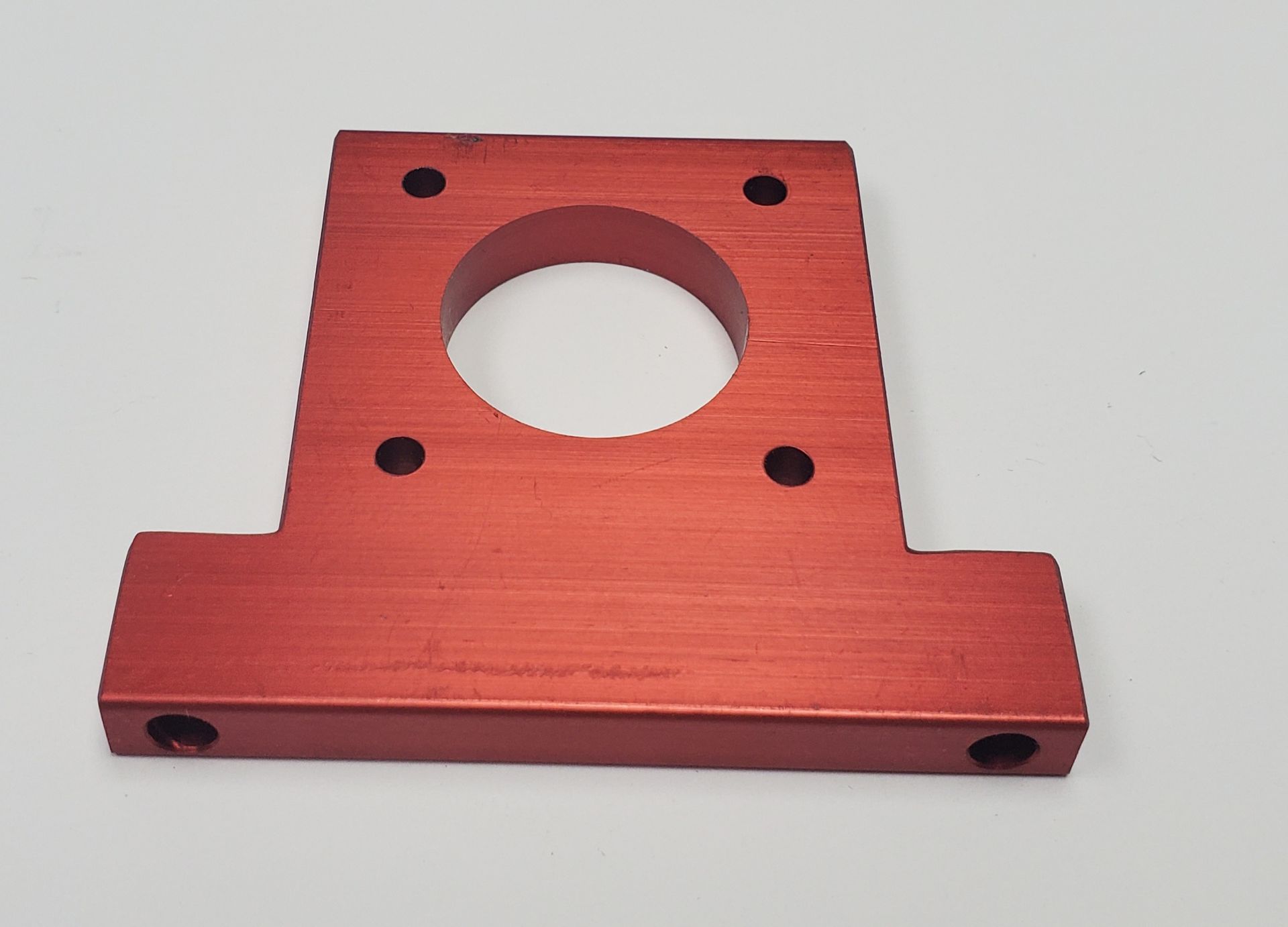 A red anodized aluminum motor mount bracket with a central circular cutout and four mounting holes on a white background.