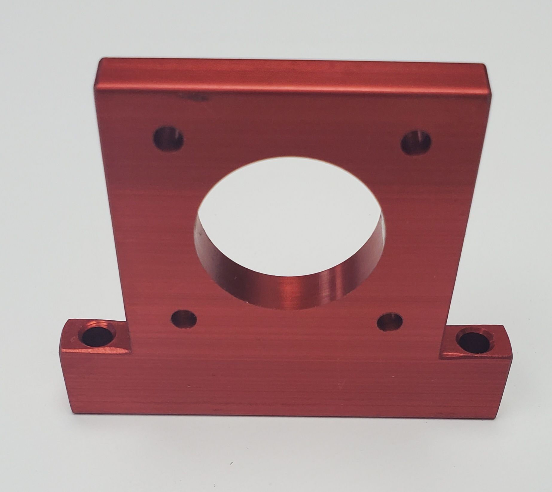 A red, T-shaped aluminum motor mount bracket with a large center hole and four bolt holes.