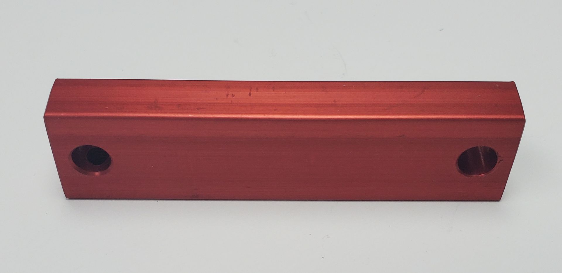 A rectangular, red aluminum bar with a circular hole at each end, shown against a plain white background.