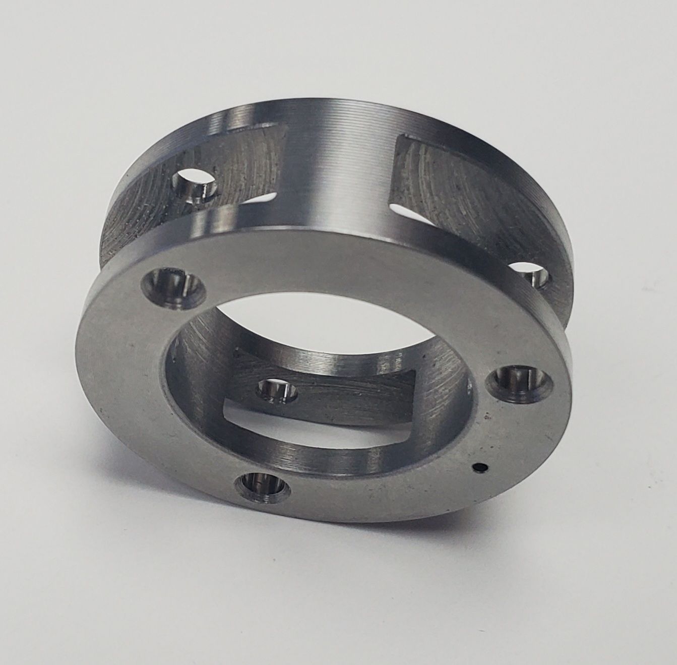 A circular metal mechanical component with a central opening, four bolt holes, and cut-out sections on the sides.