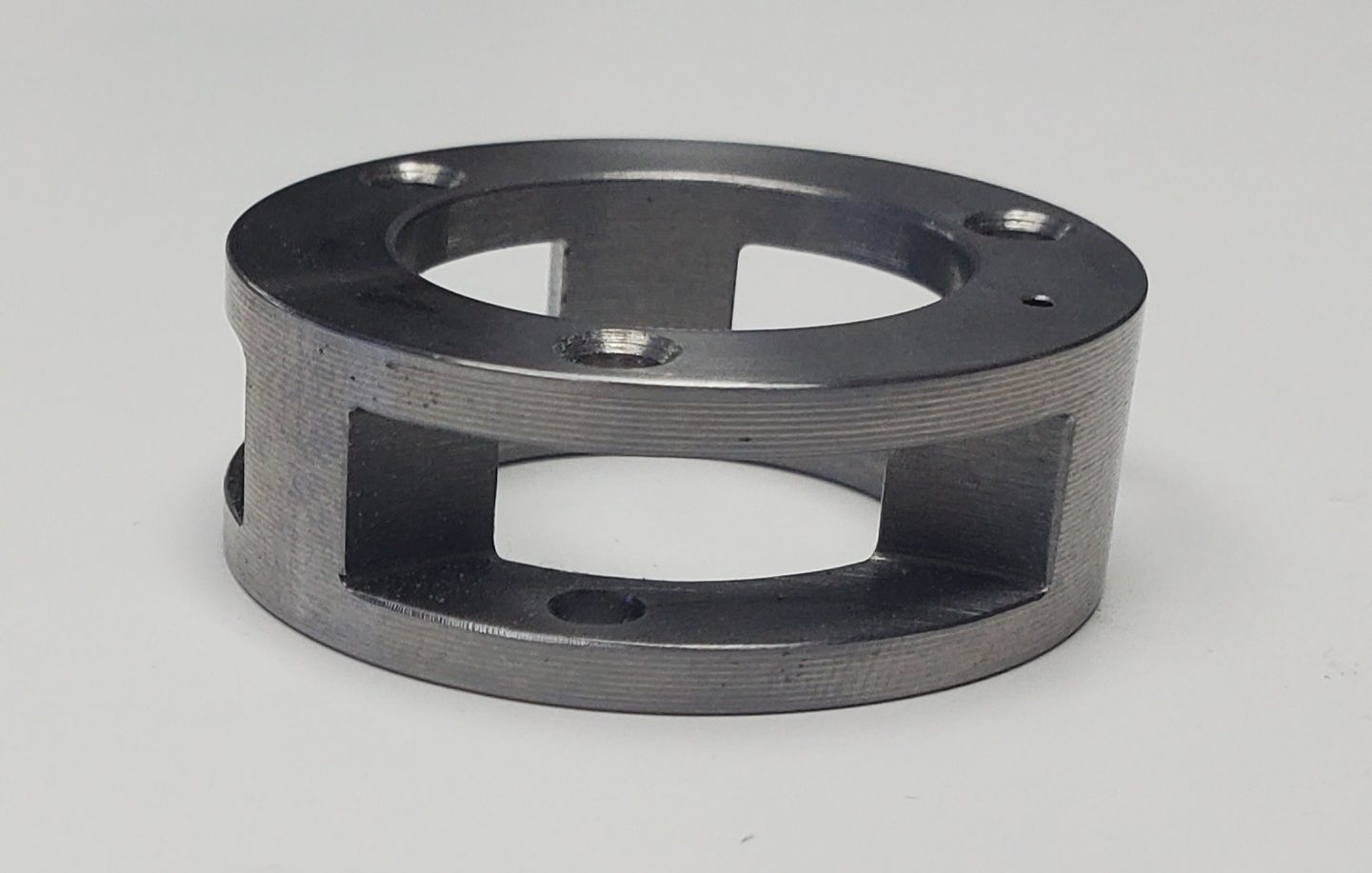 A metallic, cylindrical cage-like component with circular top flanges and open rectangular side ports on a white background.