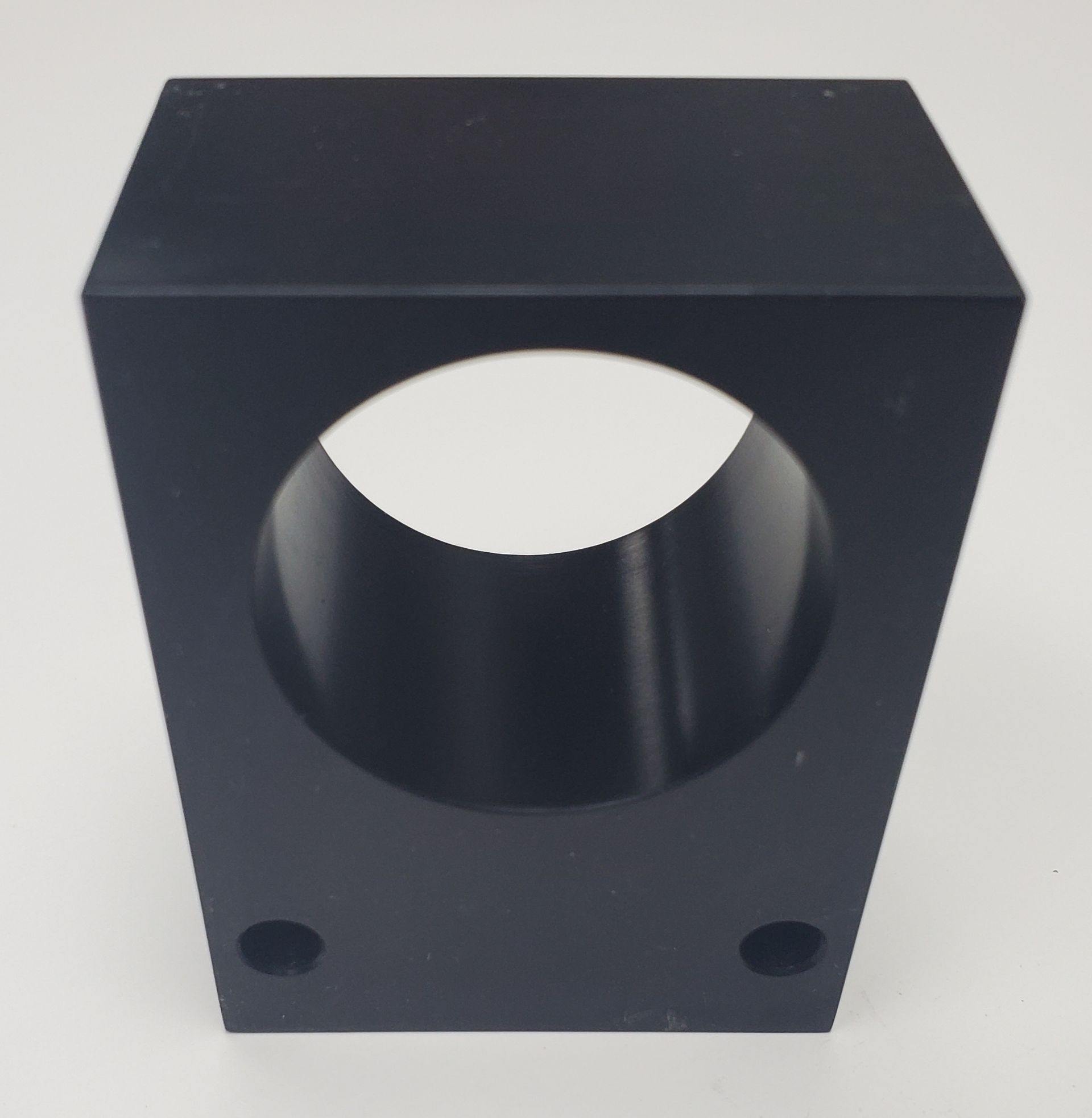 A black, rectangular mechanical block with a large circular hole in the center and two small mounting holes at the base.