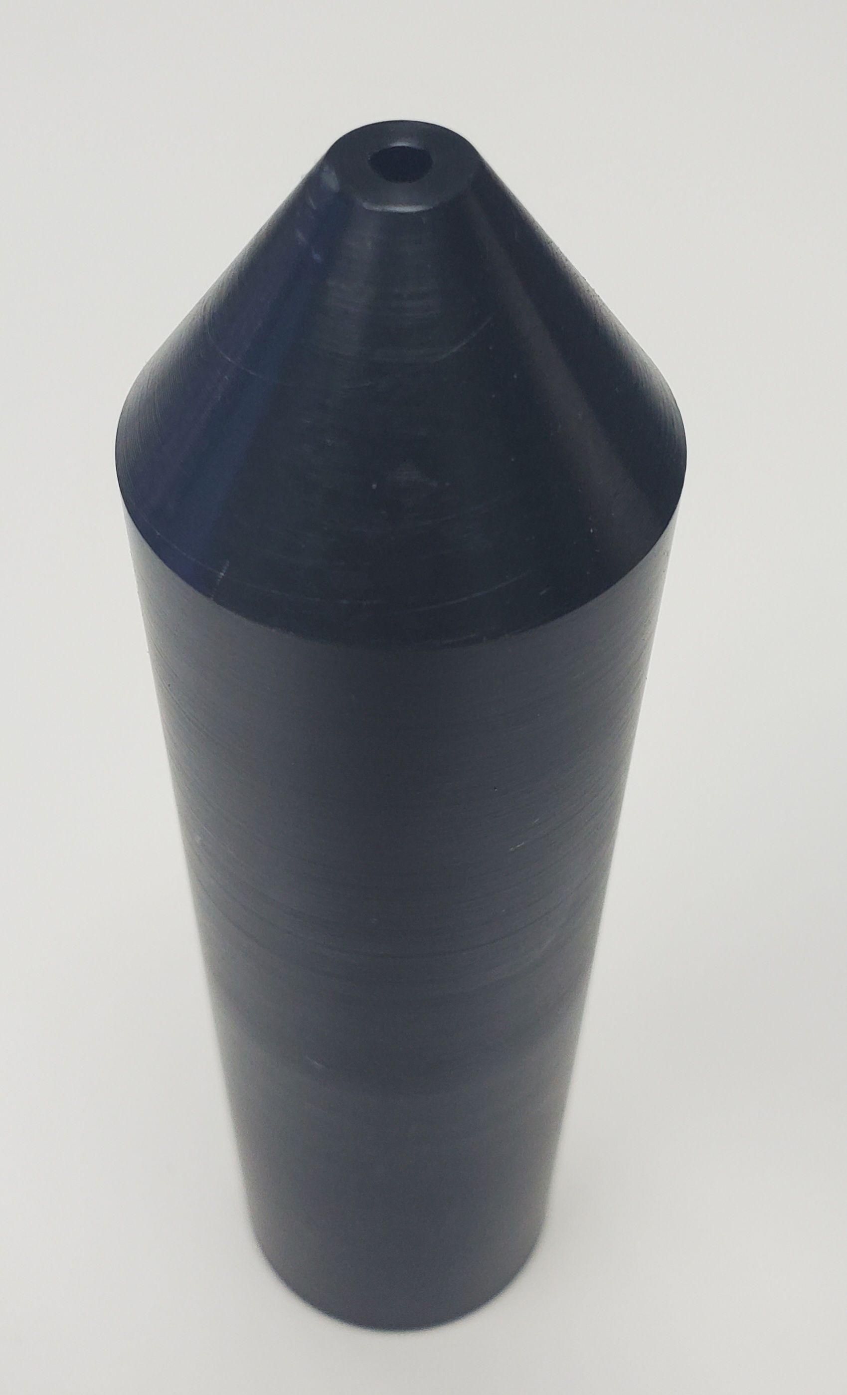A dark grey, cone-topped cylindrical plastic nozzle or cap with a small circular hole at the tip, on a white background.