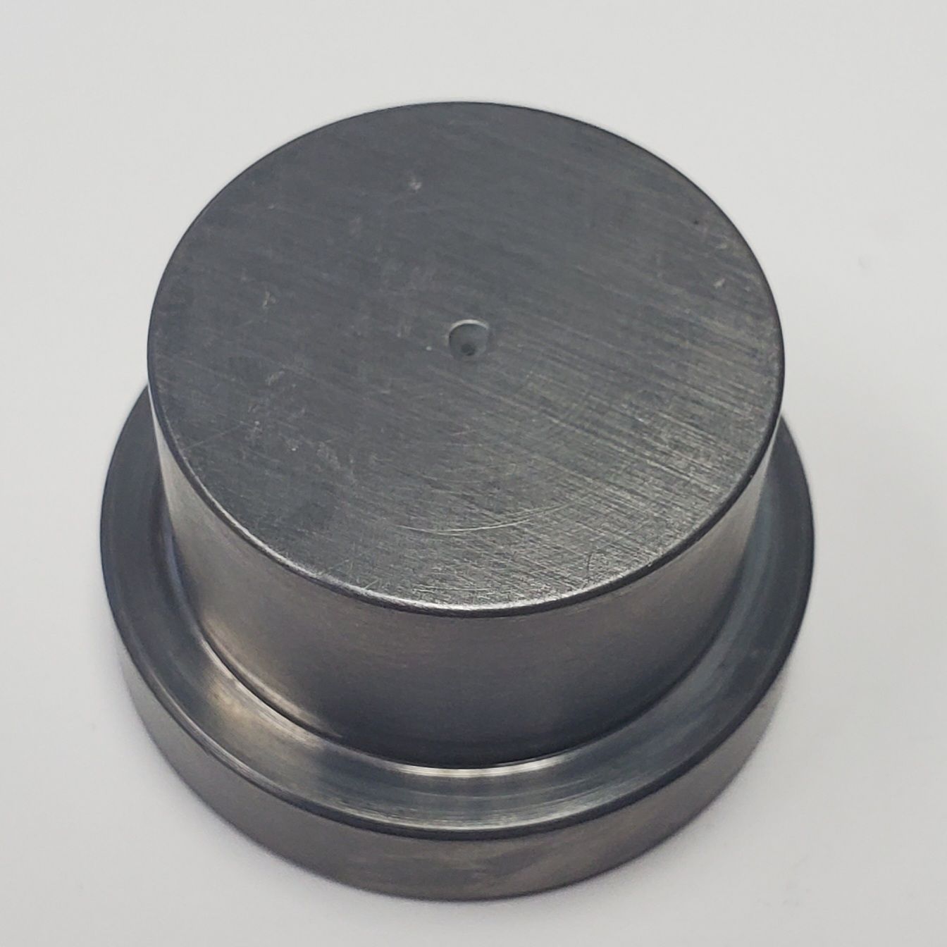 A circular, stepped industrial metal component with a smooth, dark finish and a small centered hole on top.