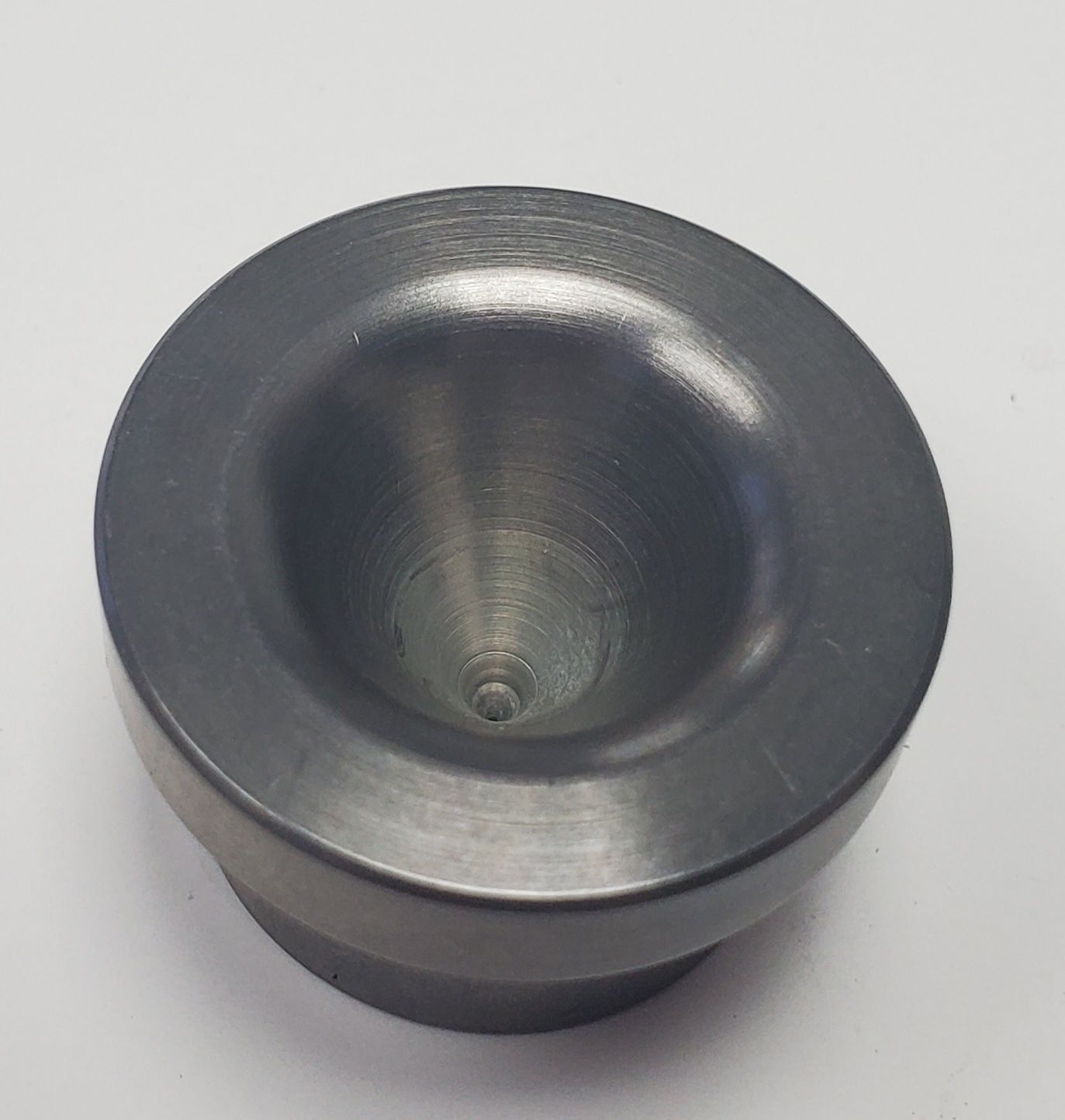 A small, cylindrical gray metal component with a smooth, concave bowl-shaped center, set against a plain white background.