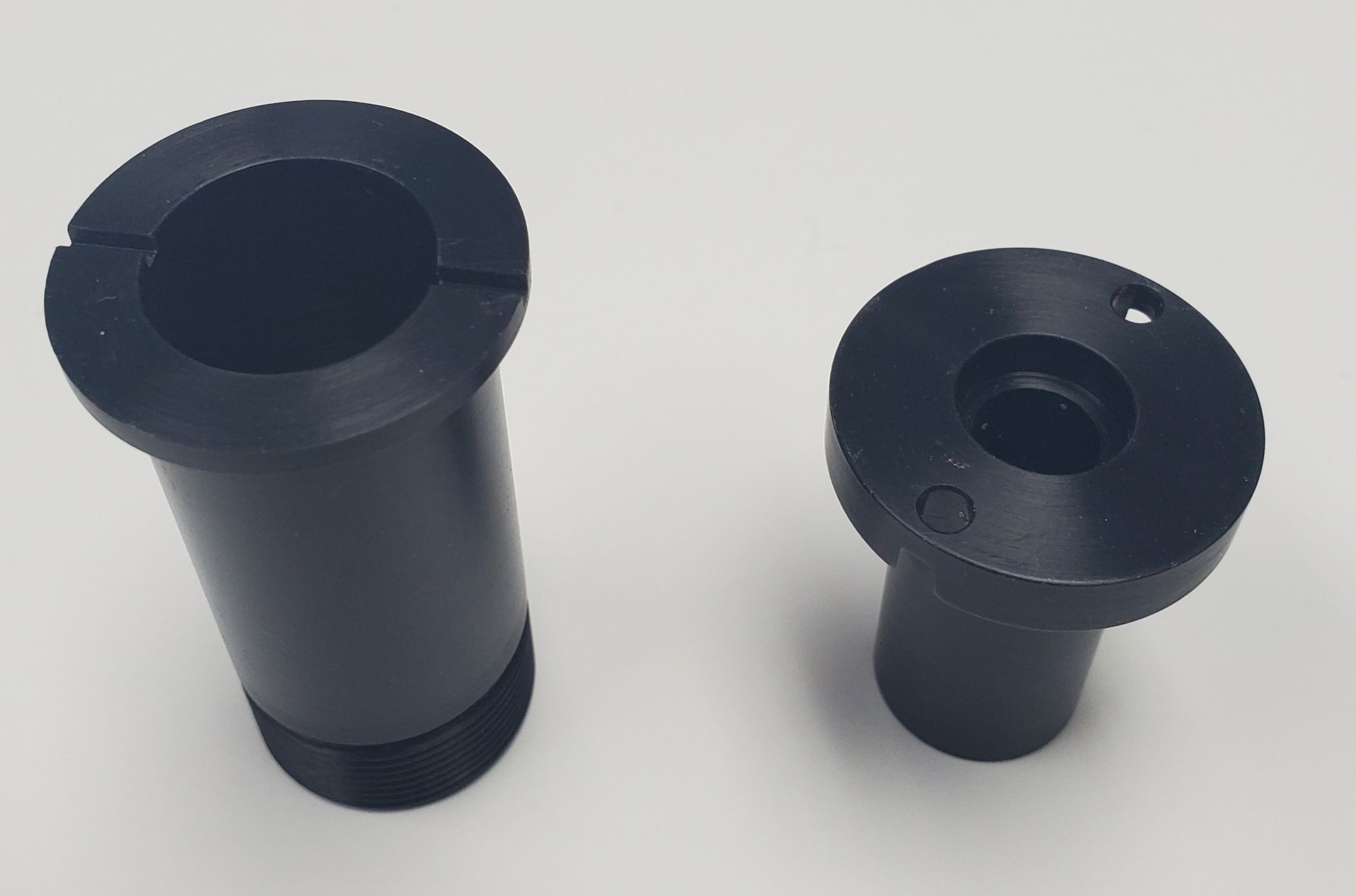 Two cylindrical black machined metal parts placed side-by-side against a plain white background.