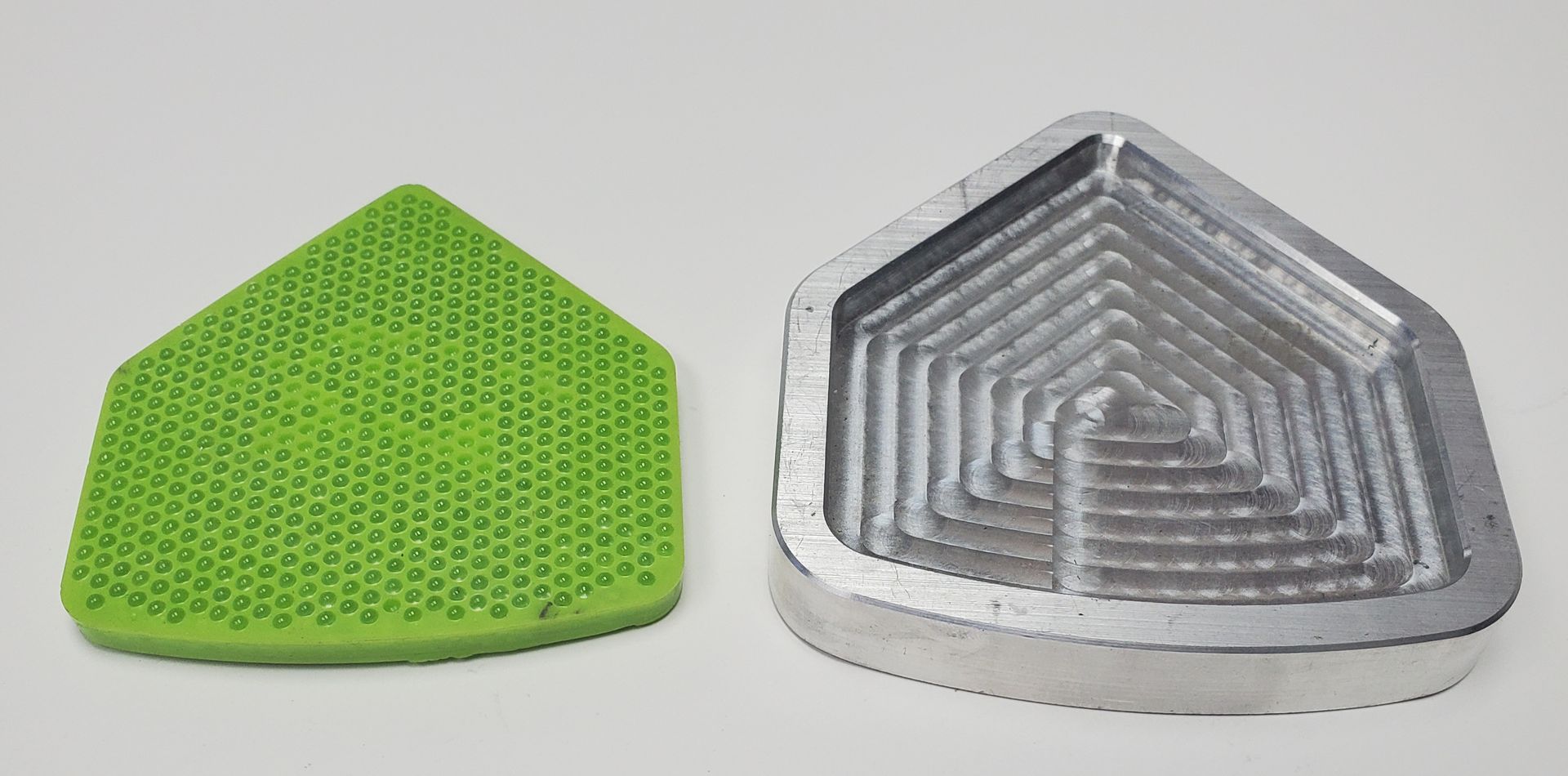 A green, textured pentagonal insert beside a matching silver, machined metal pentagonal mold on a white background.
