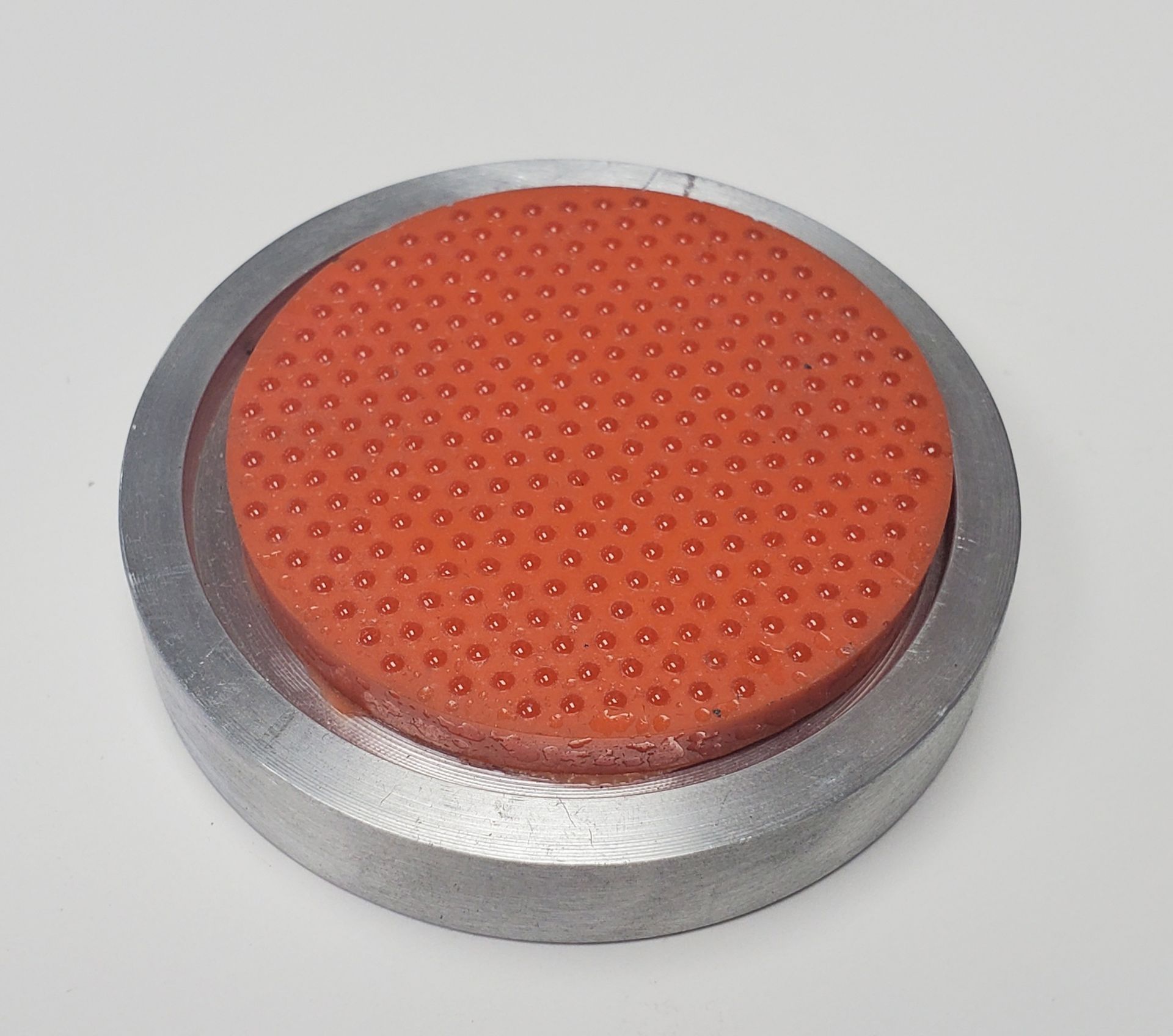 A textured, circular orange silicone pad set into a metallic gray cylindrical base, centered on a plain white background.