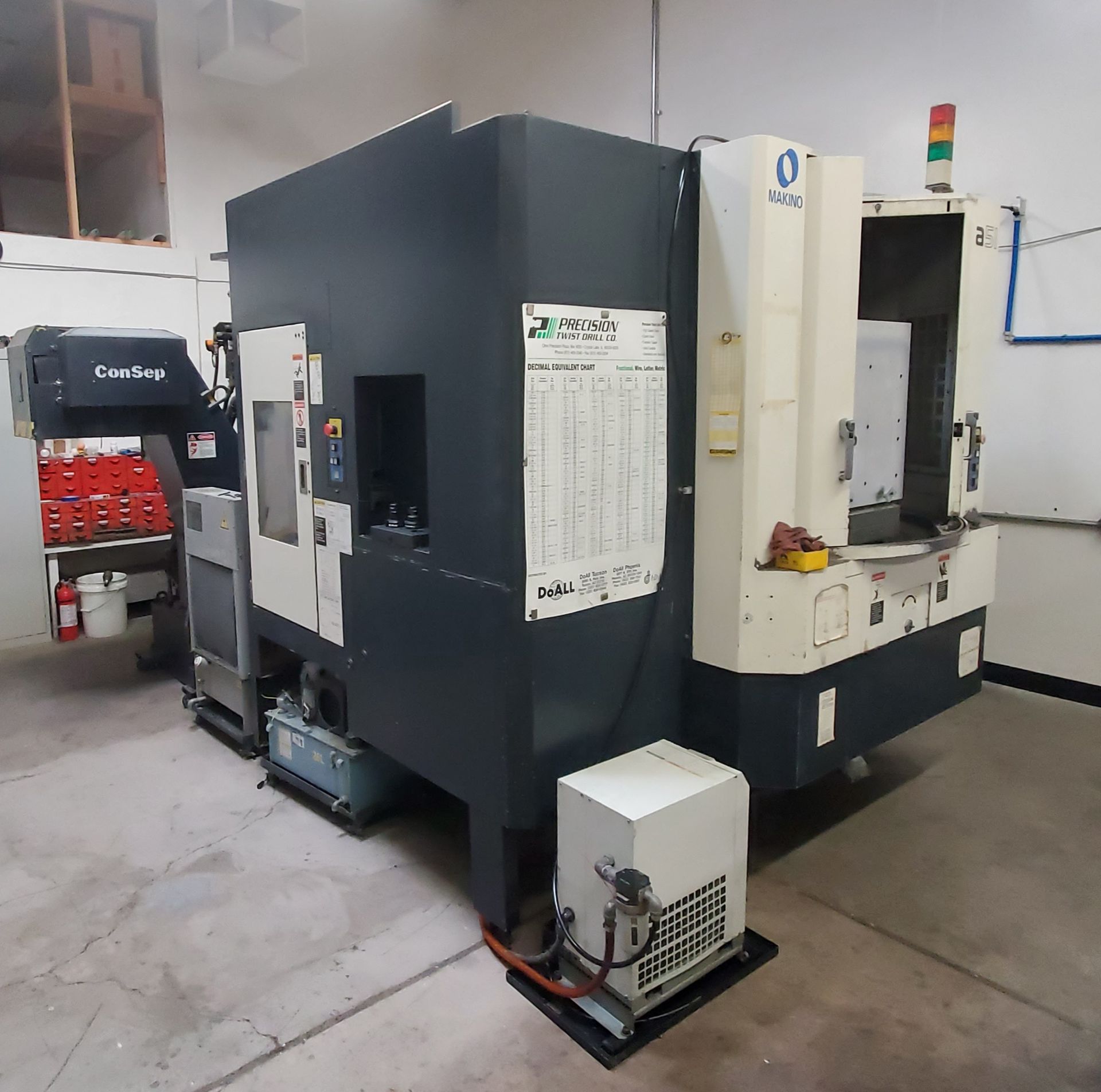A large, industrial CNC milling machine in a workshop with a grey and white exterior and a side-mounted coolant system.