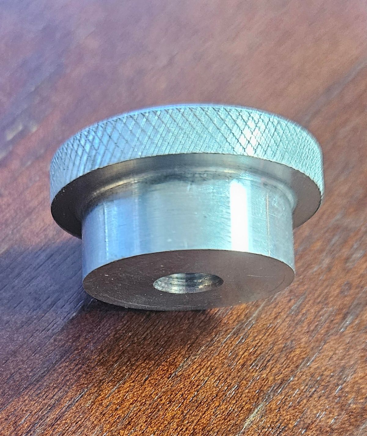 A metallic, knurled-edge adjustment knob with a threaded central hole, resting on a wooden surface.