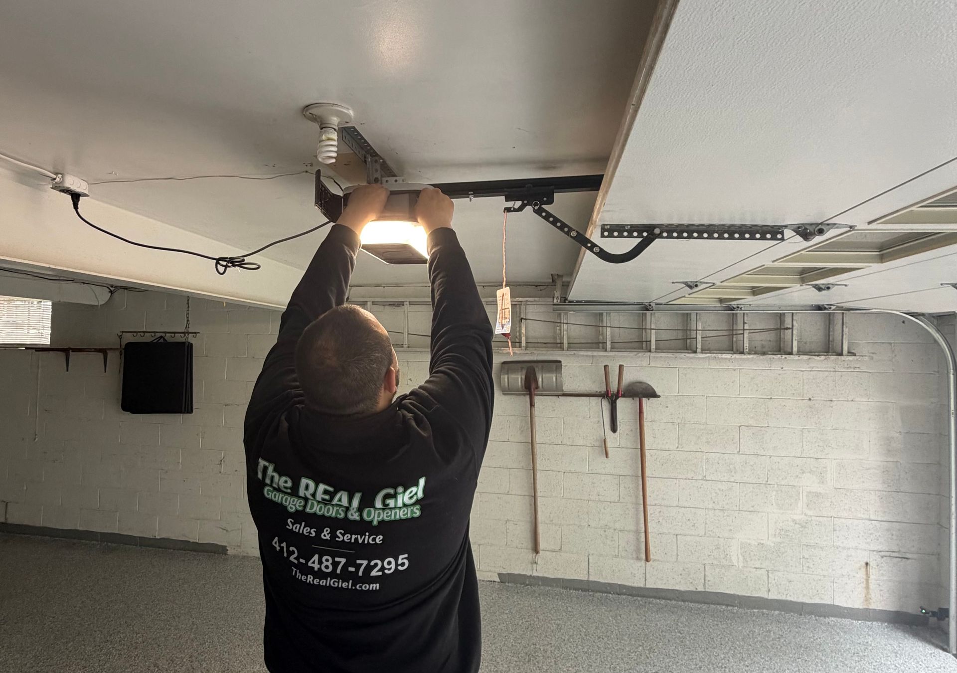 Person tightening a ceiling-mounted light fixture in a garage-like room with white brick walls