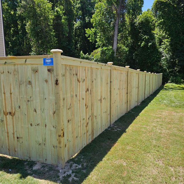 Wooden privacy fence along a grassy yard with trees in the background