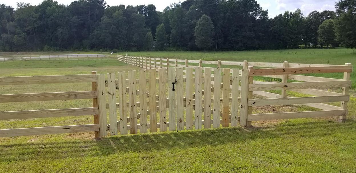 Wooden fence gate in a grassy field with trees in the background