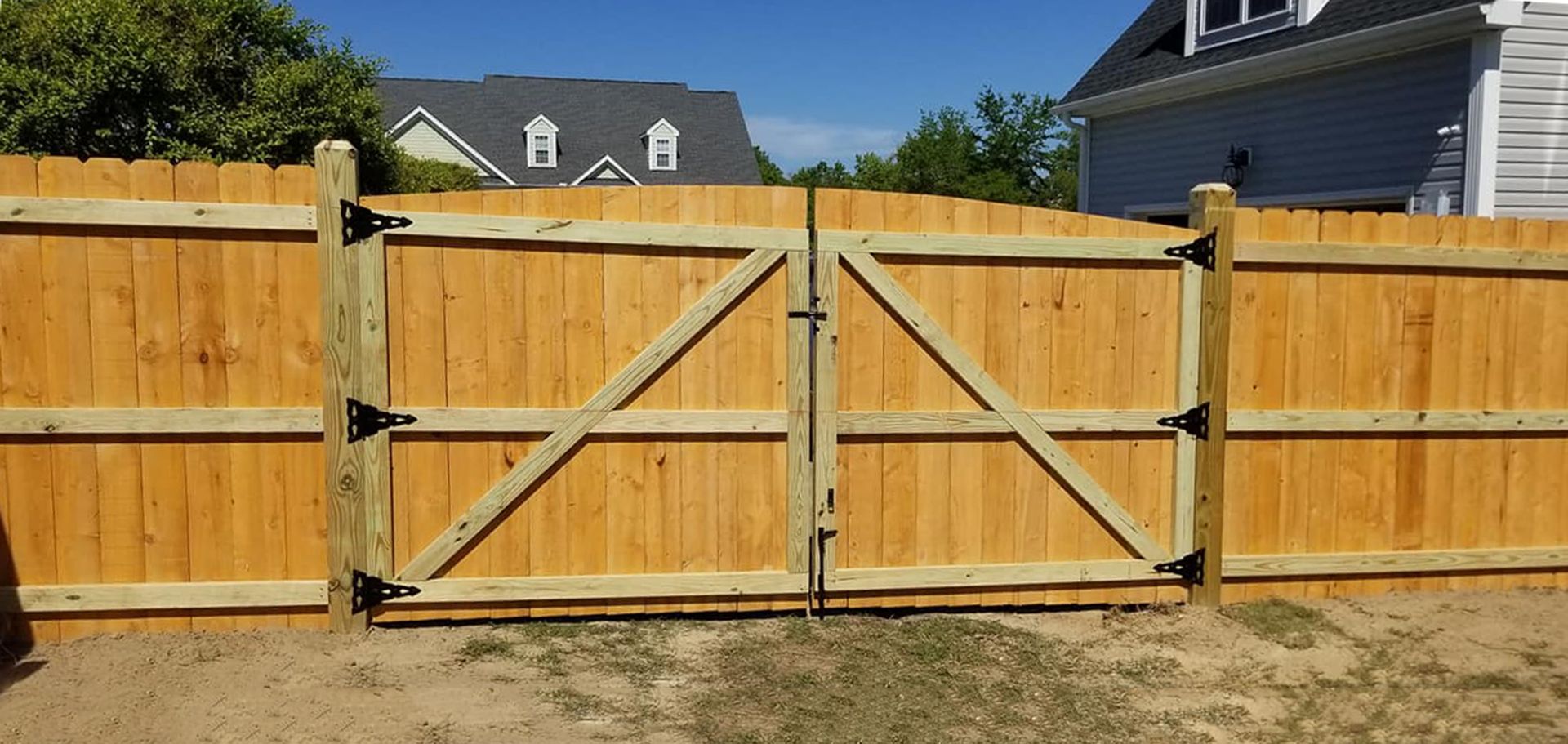 Wooden double driveway gate with diagonal braces in a fenced backyard under a clear blue sky