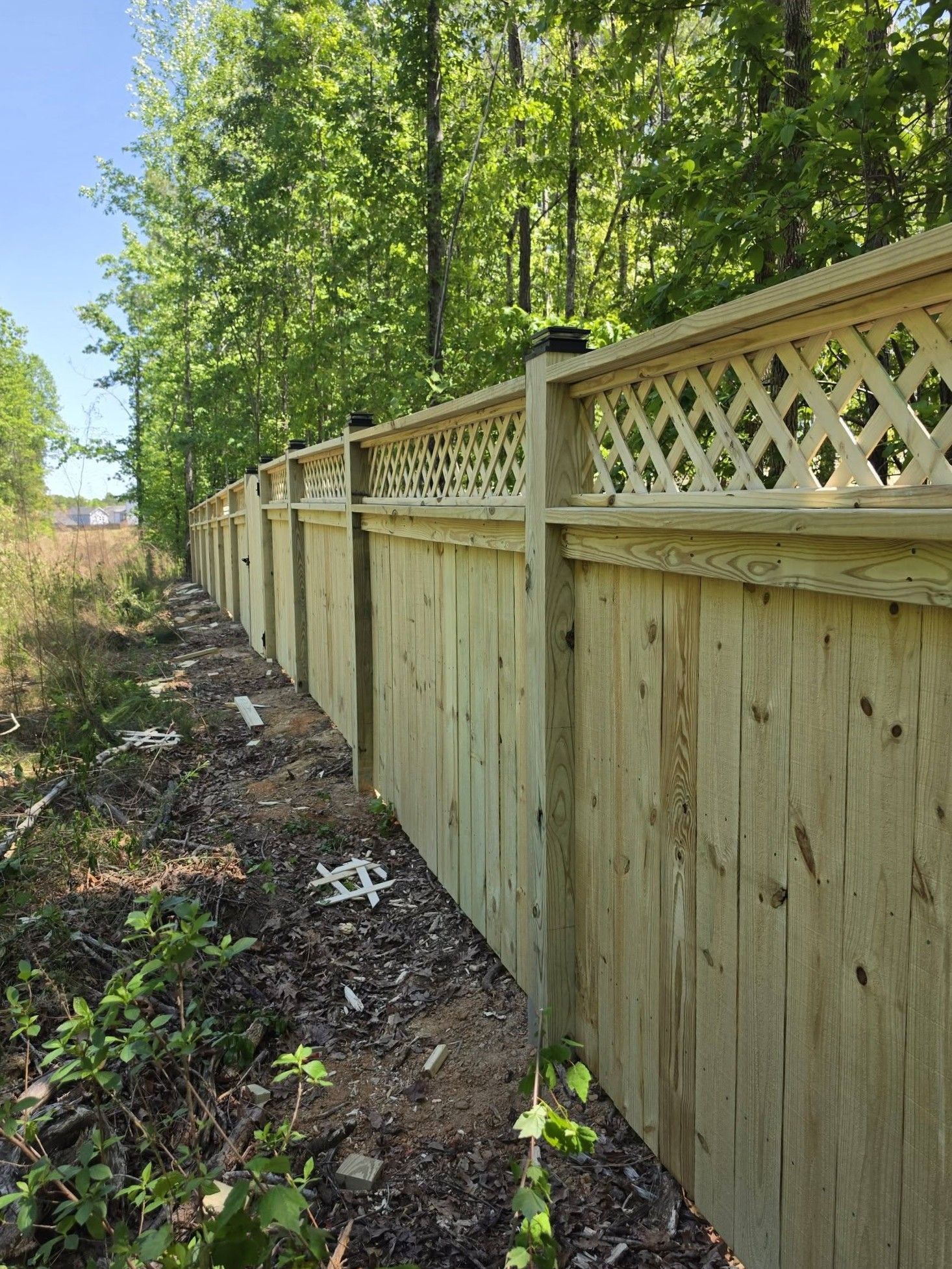 Wooden privacy fence with lattice top along a leafy wooded path