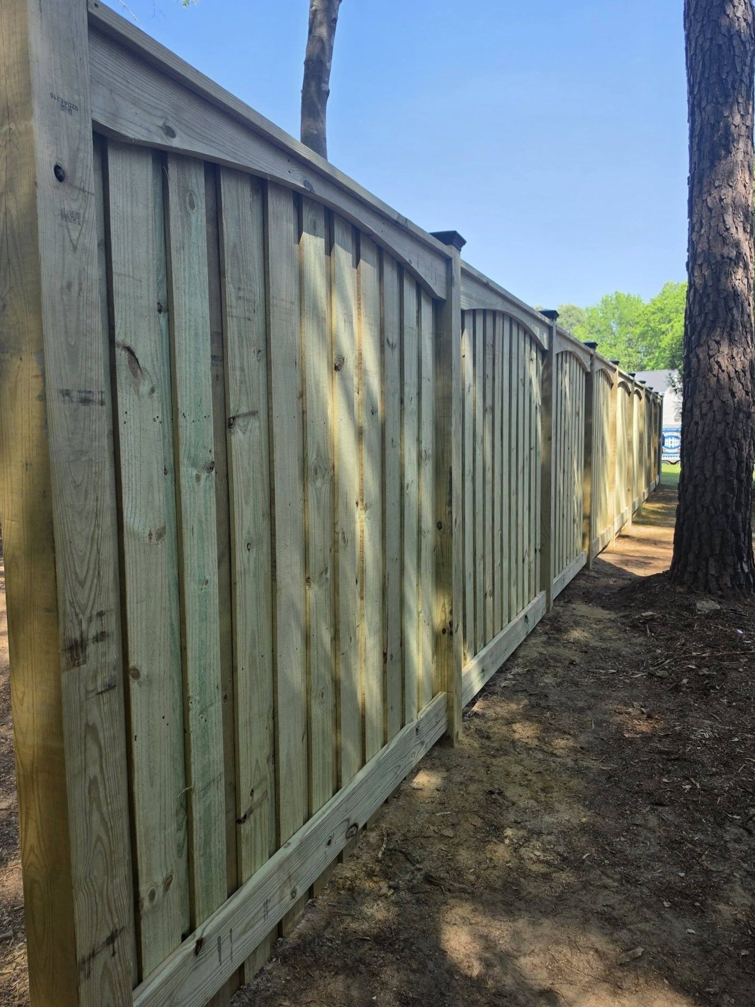 Wooden fence along a narrow dirt path beside trees and a house