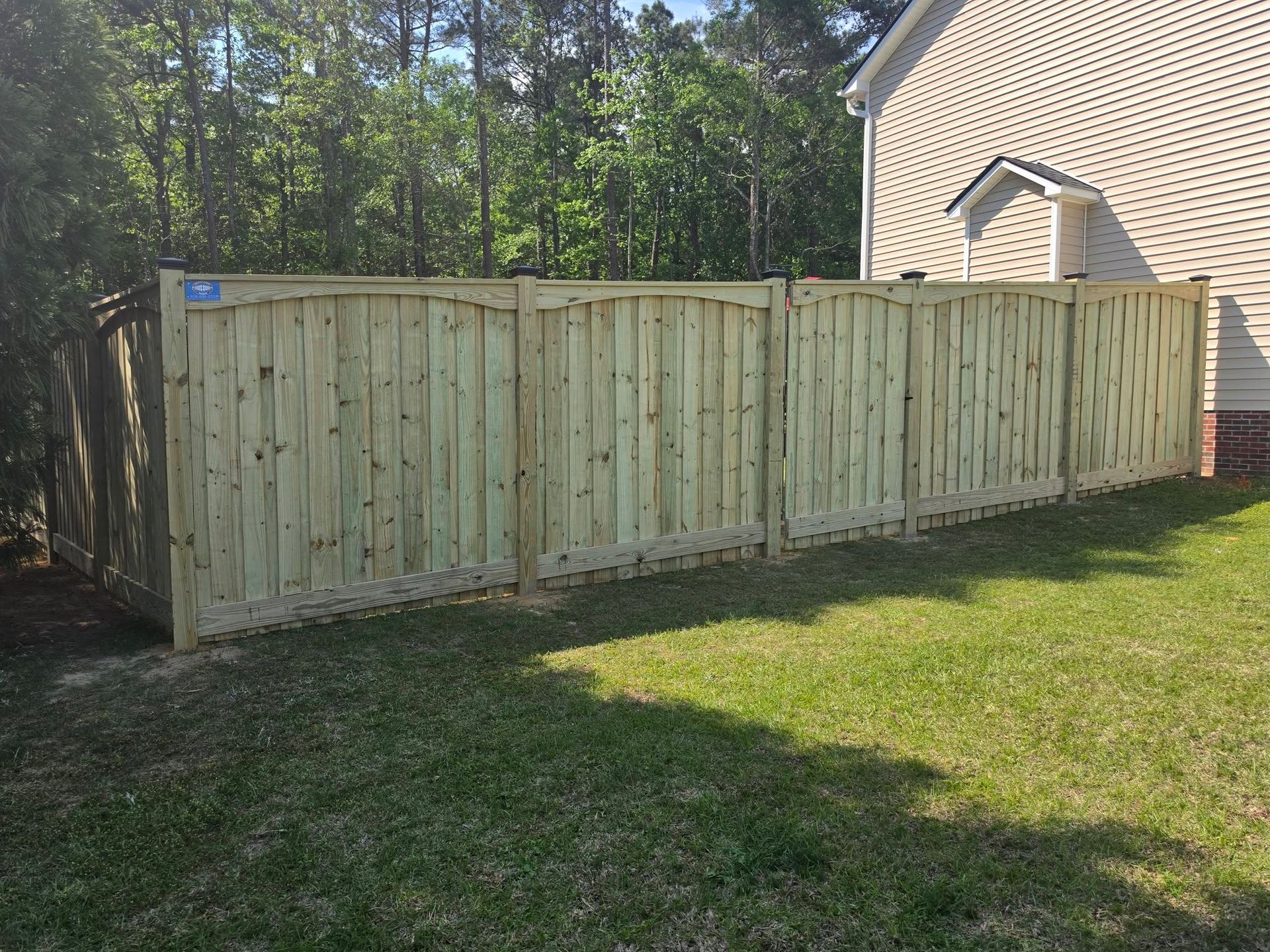 Wooden privacy fence along a grassy yard beside a beige house and trees