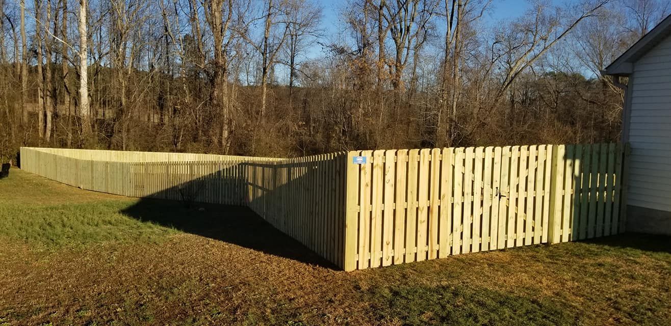 Wooden privacy fence enclosing a yard in autumn sunlight, with trees and a house beside it