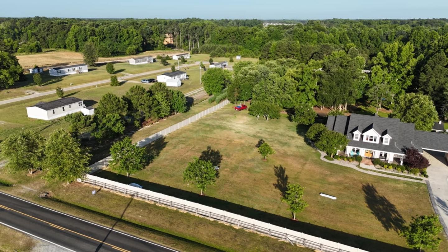 Aerial view of a rural property with a white house, lawn, road, and surrounding trees.