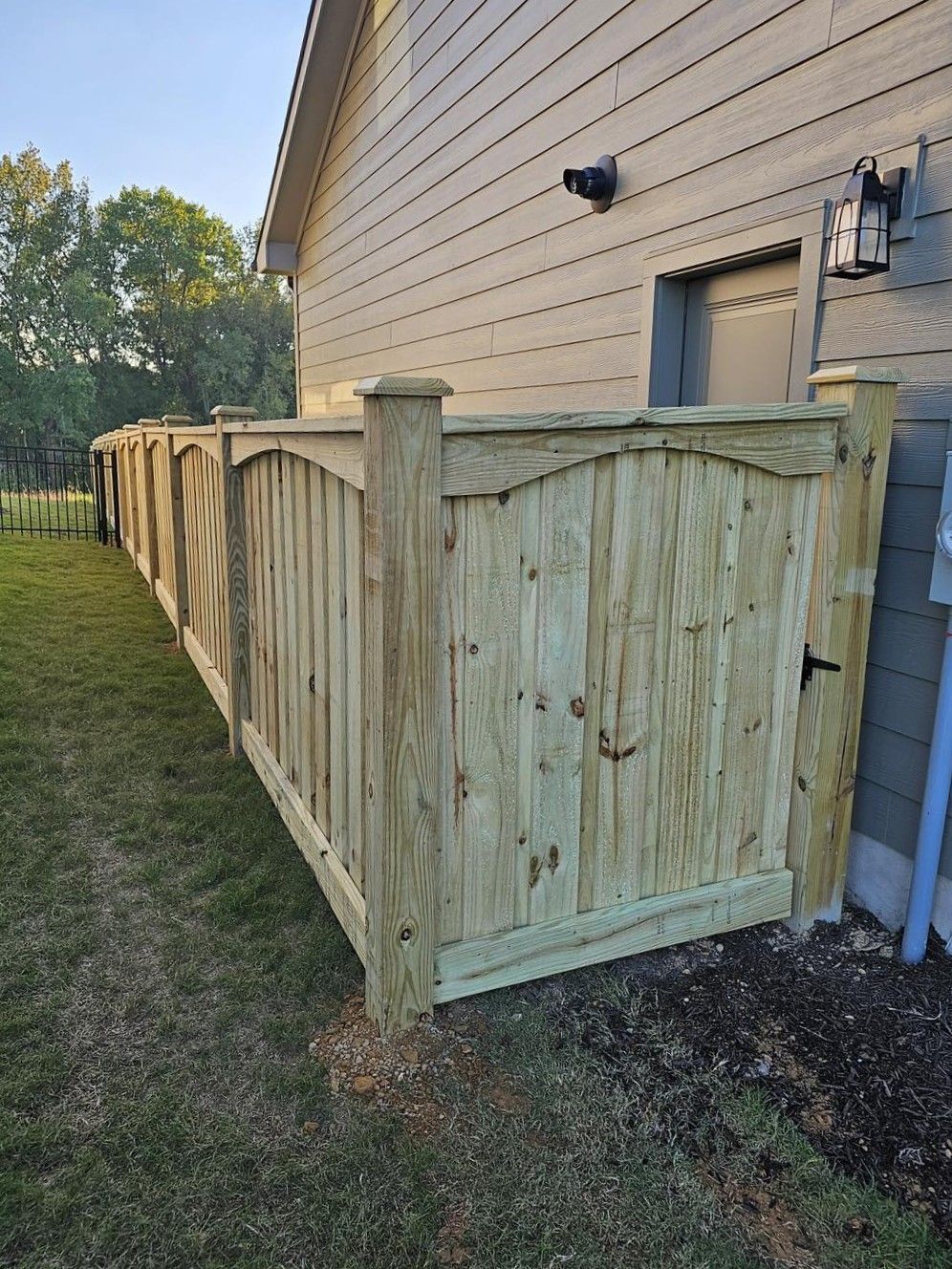 Wooden privacy fence and gate along the side of a beige house, beside a grassy yard.