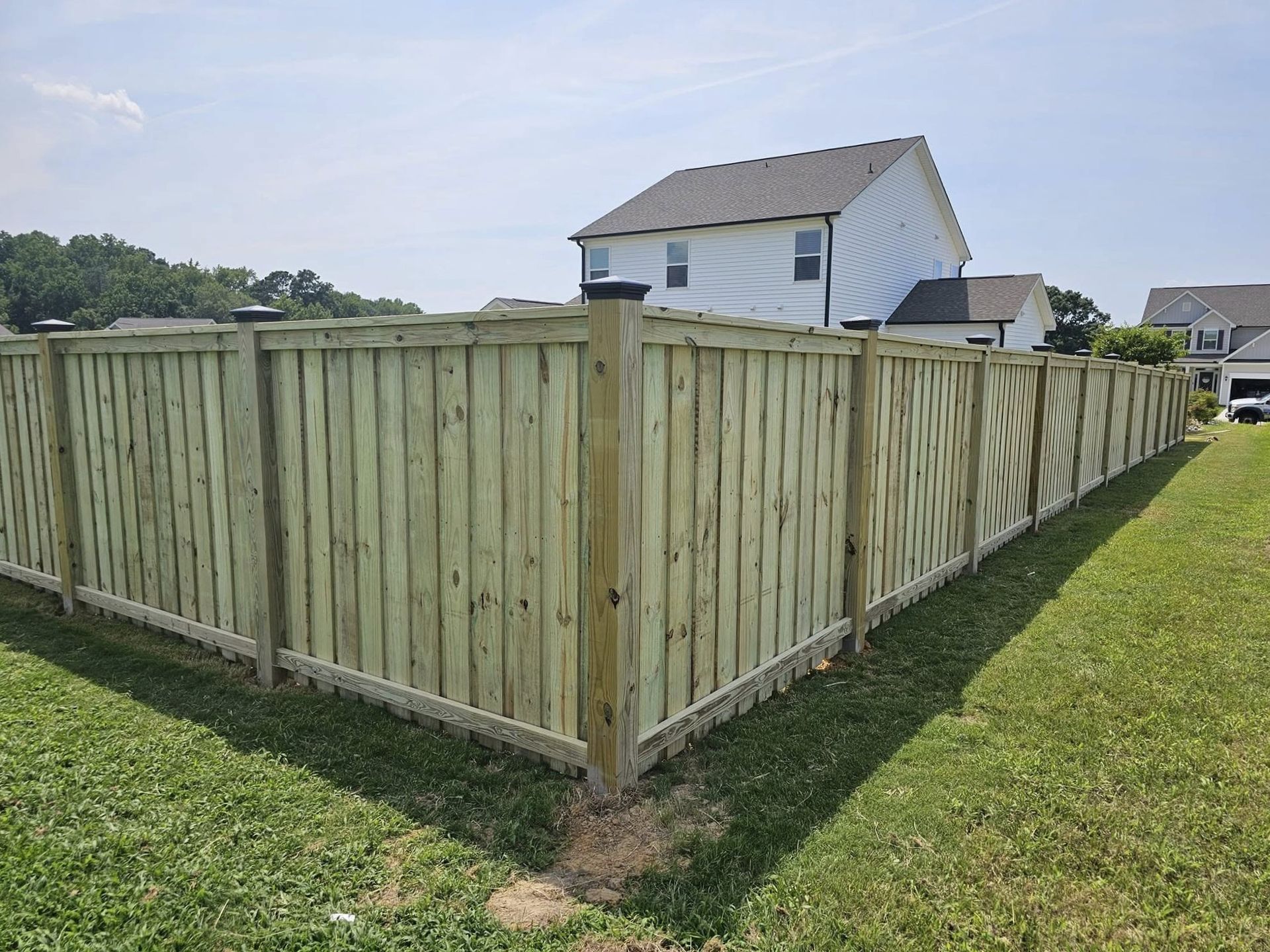 Wooden privacy fence enclosing a grassy backyard beside suburban houses on a sunny day