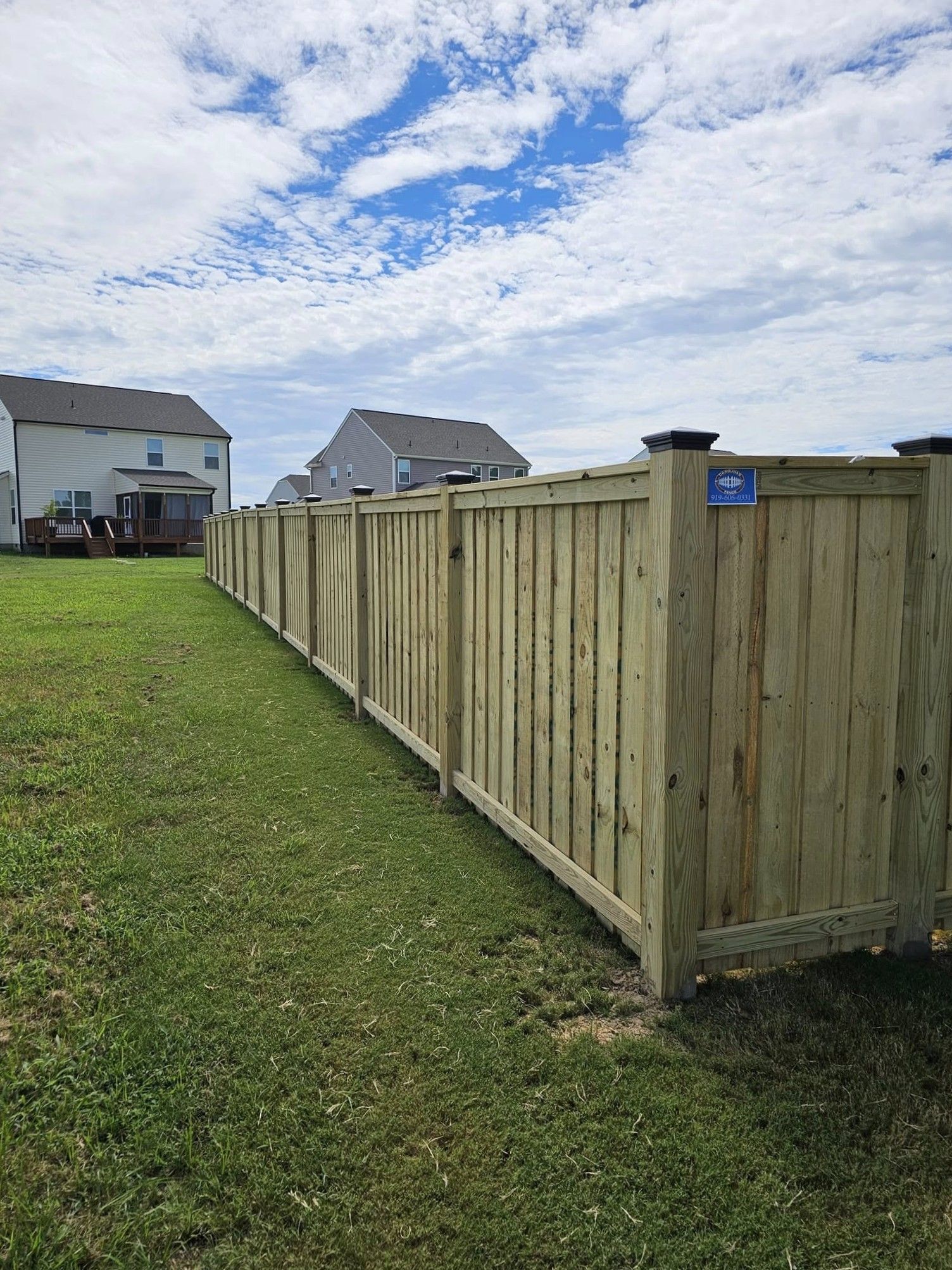 Wooden privacy fence along a grassy yard beside suburban houses under a cloudy sky
