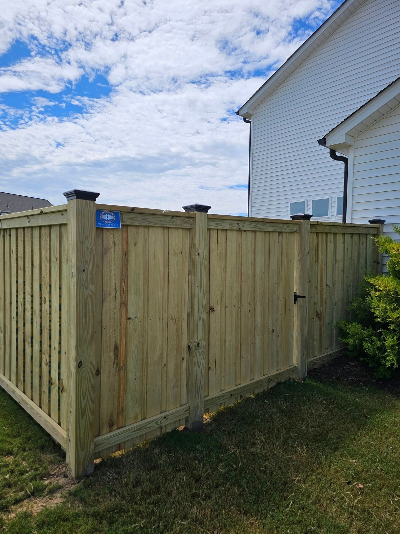 Wooden privacy fence beside a white house under a cloudy blue sky
