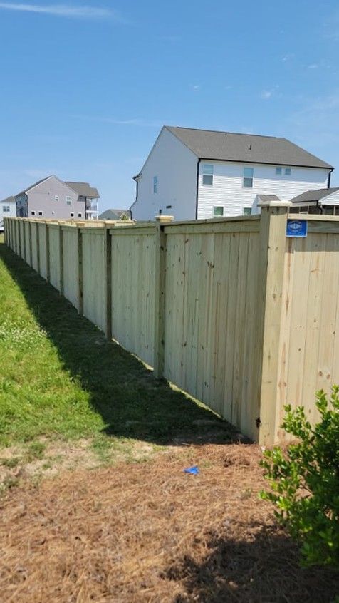 Wooden privacy fence along a grassy side yard beside white houses under a clear blue sky