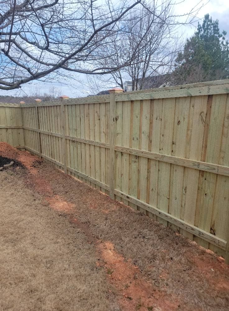 Wooden fence along a dirt path with bare tree branches and cloudy sky