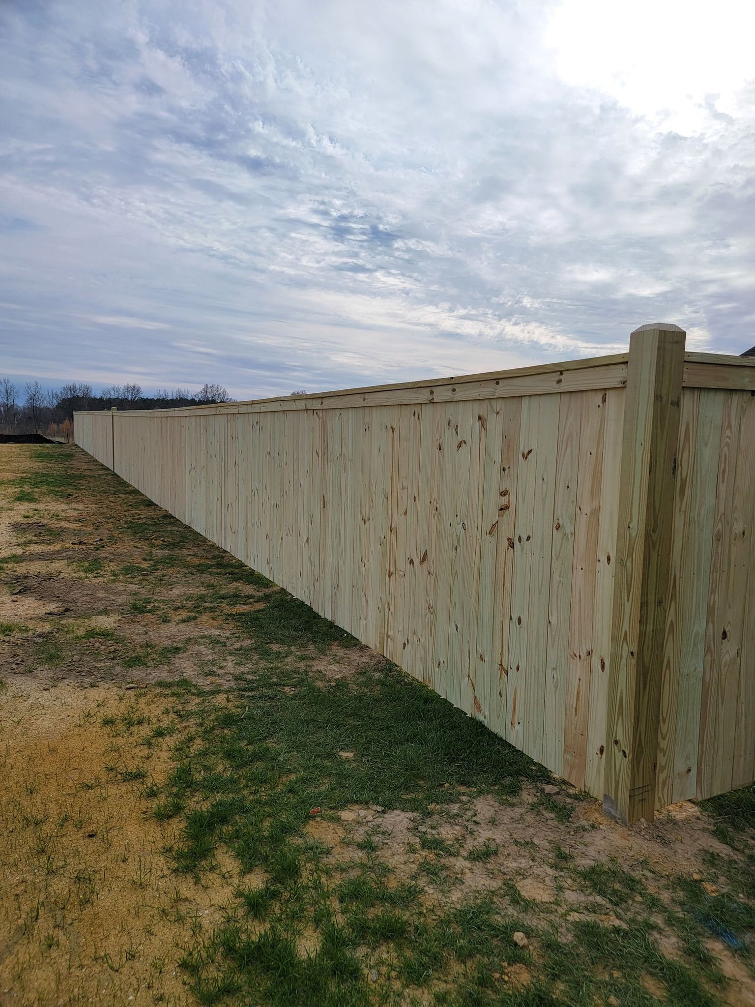 Long wooden fence along a grassy dirt path under a cloudy sky