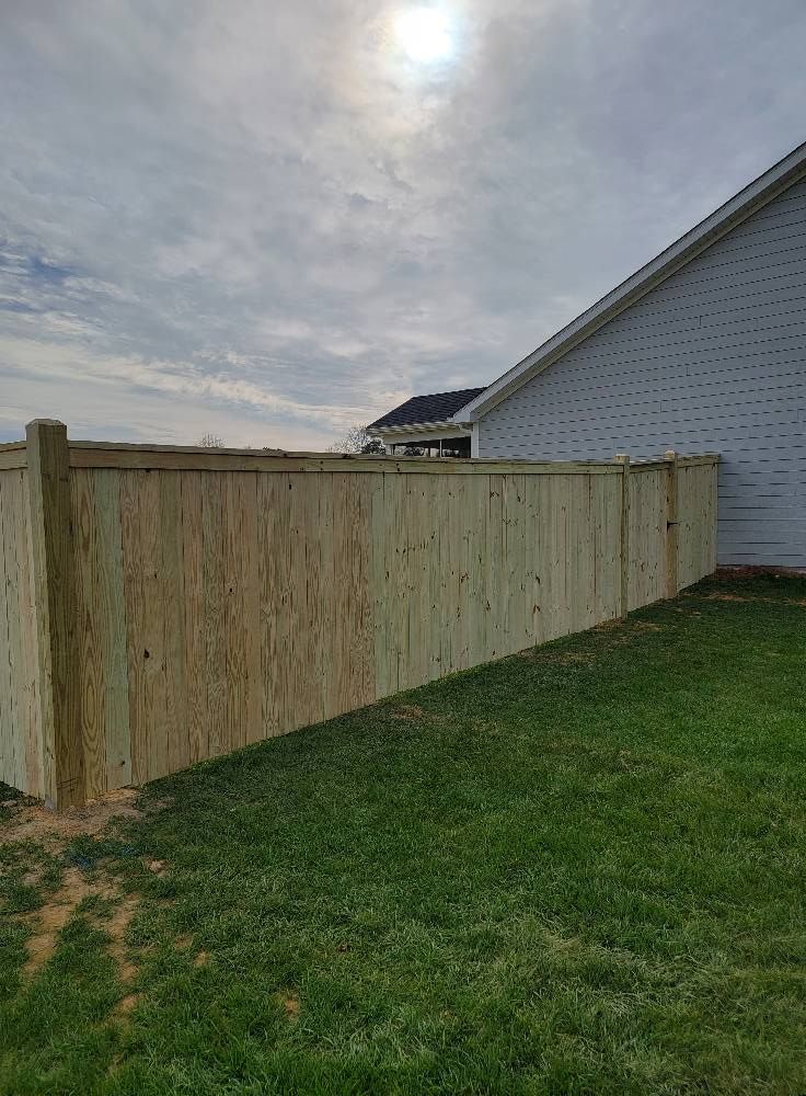 Wooden privacy fence beside a white house along a grassy backyard under a cloudy sky