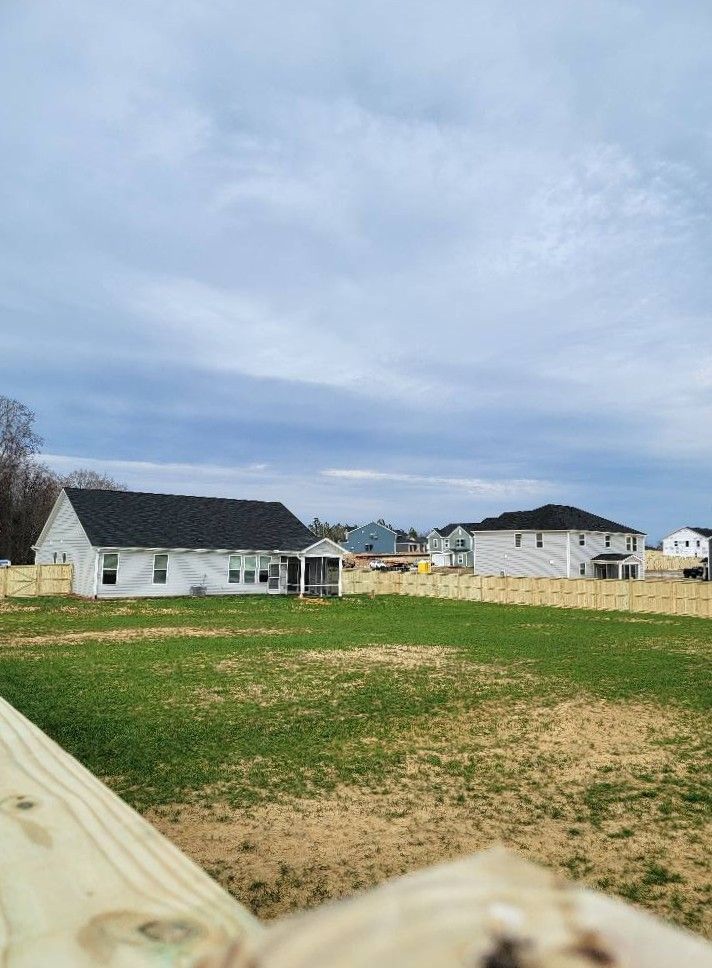 Empty grassy lot beside white houses under a cloudy sky
