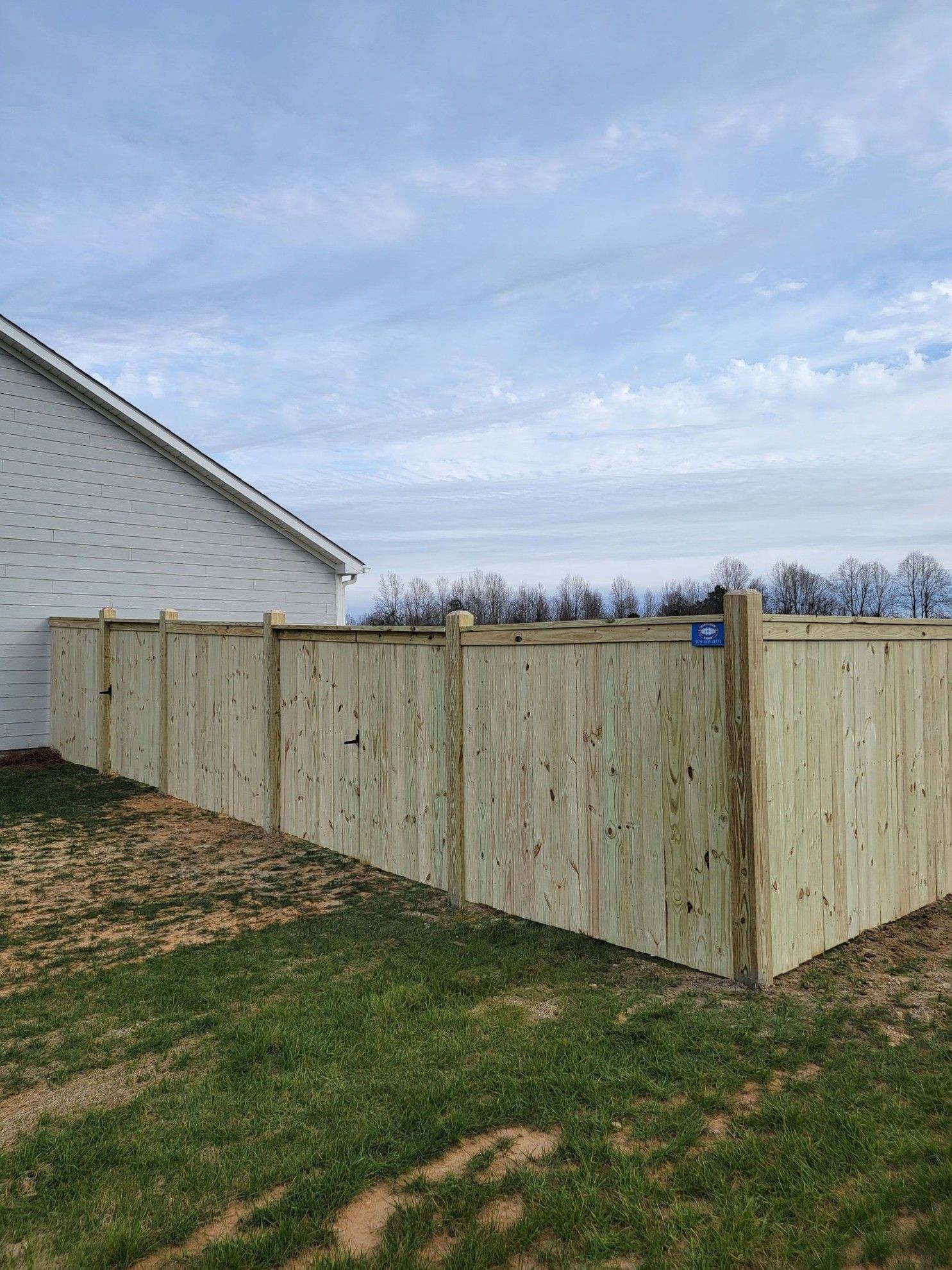 Wooden privacy fence beside a white house in a grassy yard under a cloudy sky