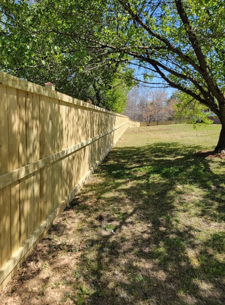 Wooden fence beside a grassy yard with trees casting dappled shade